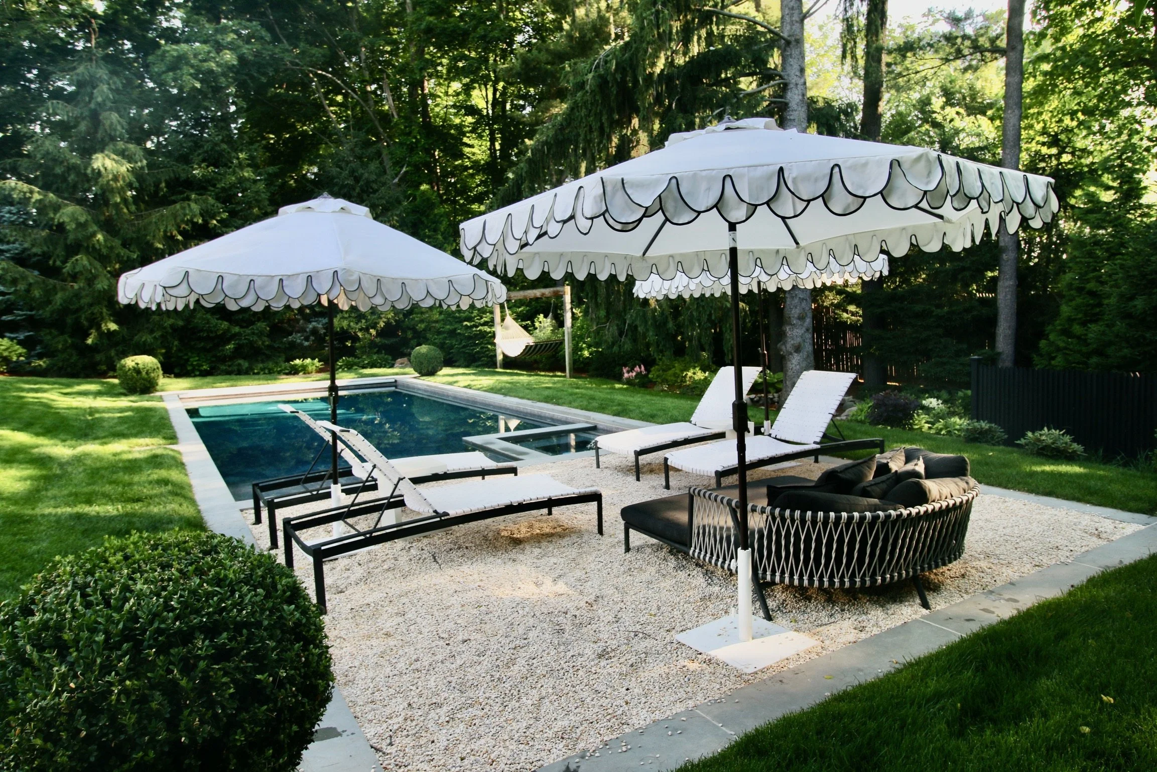 Gravel patio with scalloped white umbrellas and chaises beside the pool