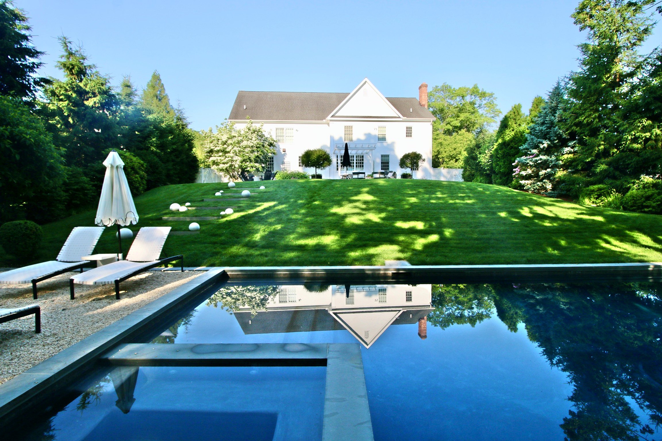 Pool reflecting the white house across a sunny lawn