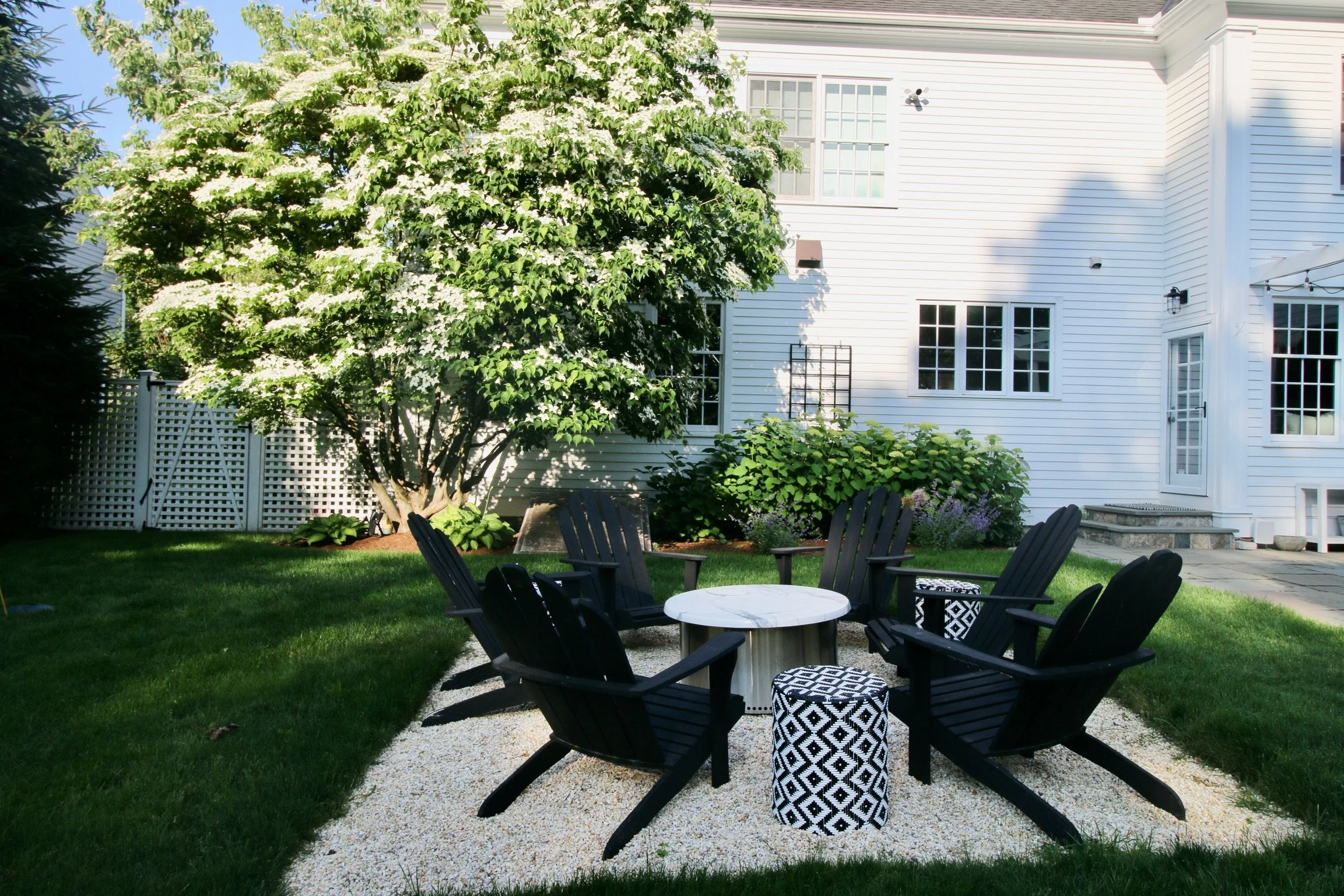 Fire pit with black Adirondack chairs on a gravel patio beside the house