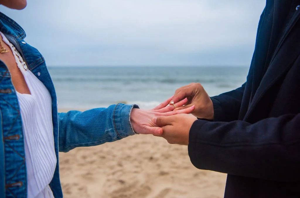 Two people at the beach holding hands with the ocean in the background.