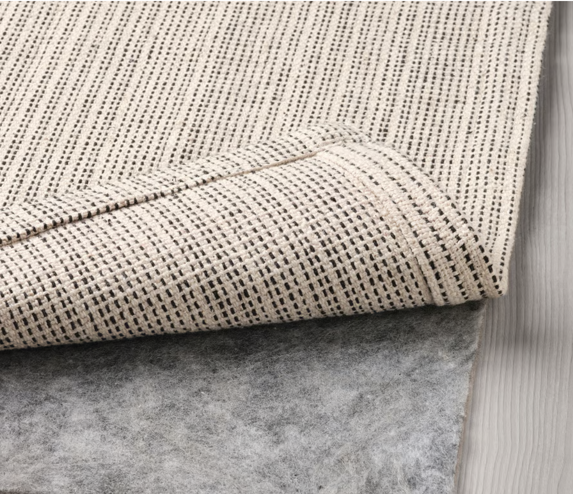 Close-up of a fabric rug with a striped pattern on a gray carpeted floor.