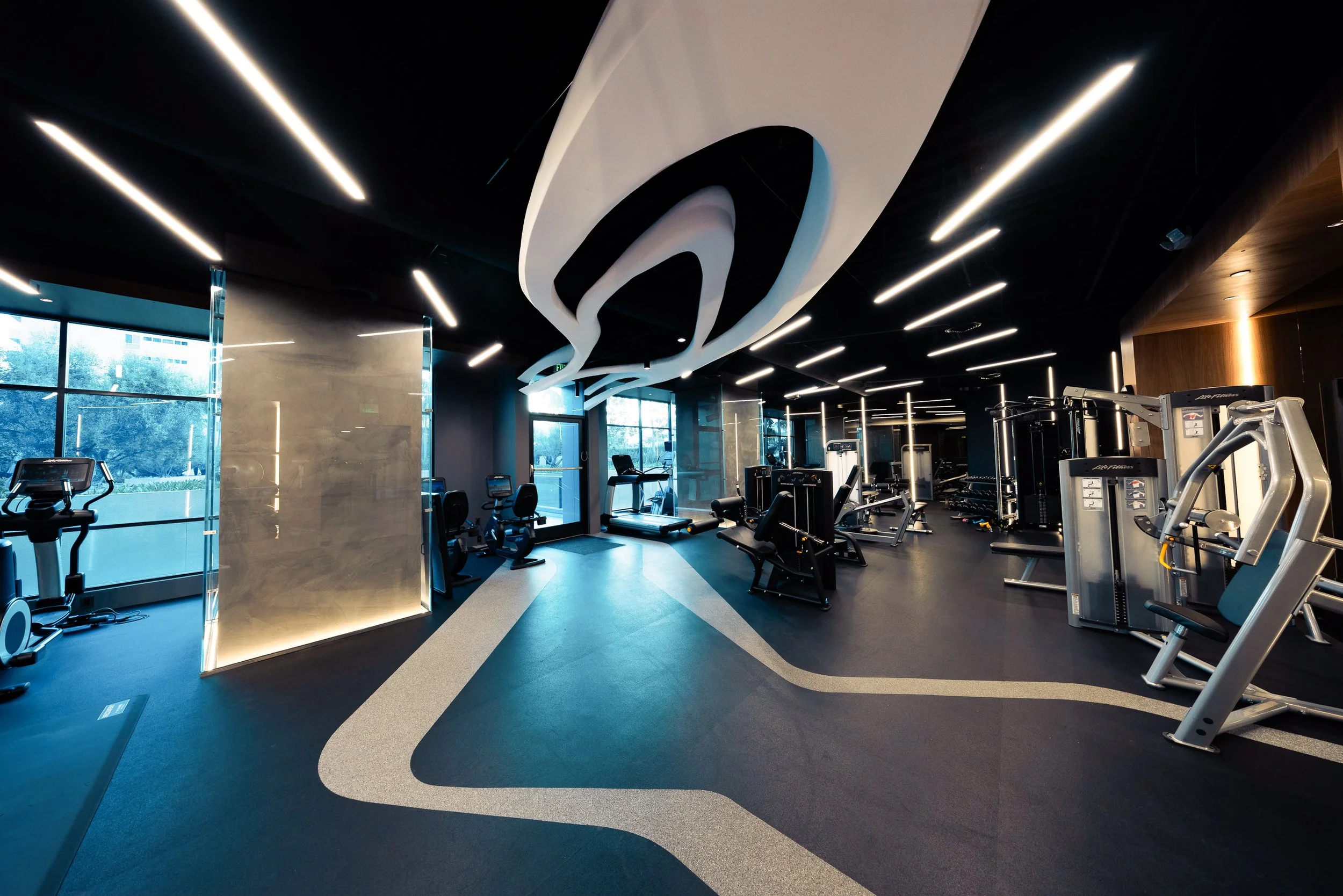 Modern gym with exercise equipment, large windows, and unique ceiling design with black and white patterns.