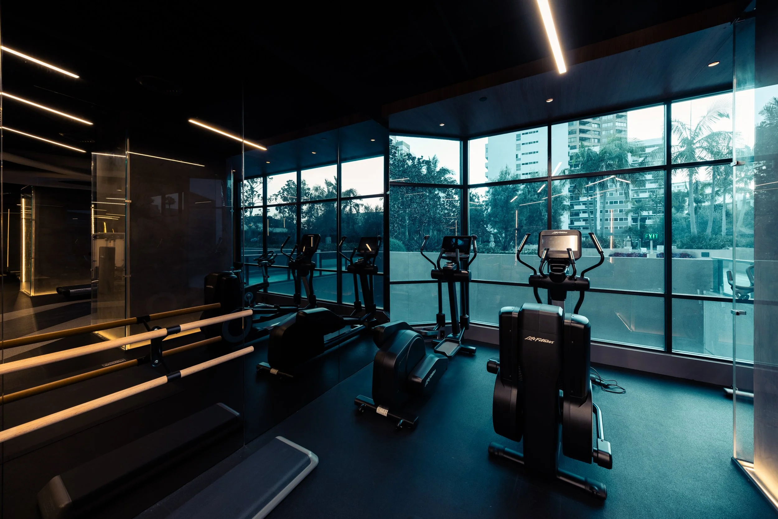 Modern gym at Blair House condominium at Westwood, Los Angeles with cardio equipment and large windows showing an urban cityscape with trees.