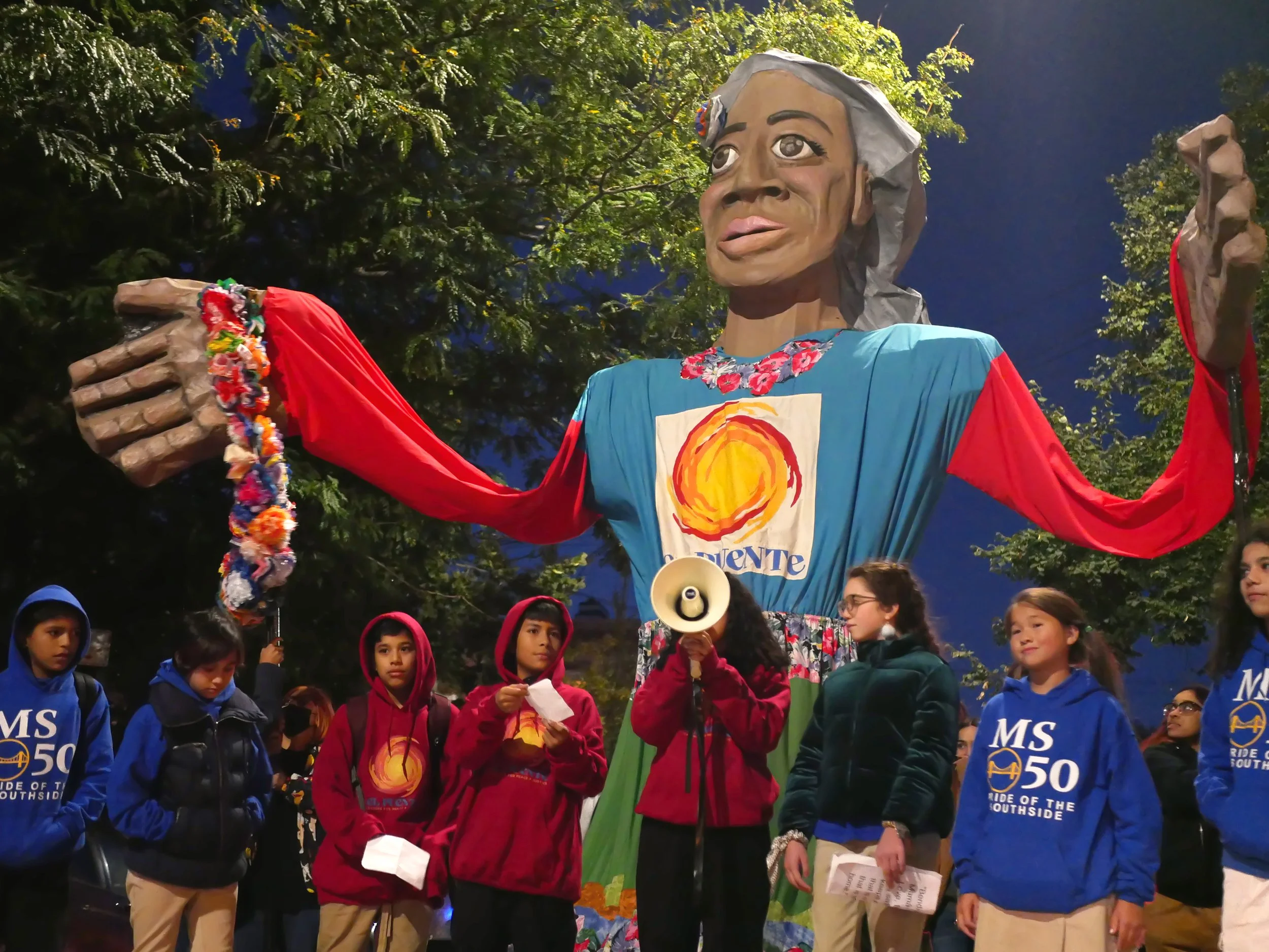 Students stand in front of large puppet, one speaking into bullhorn