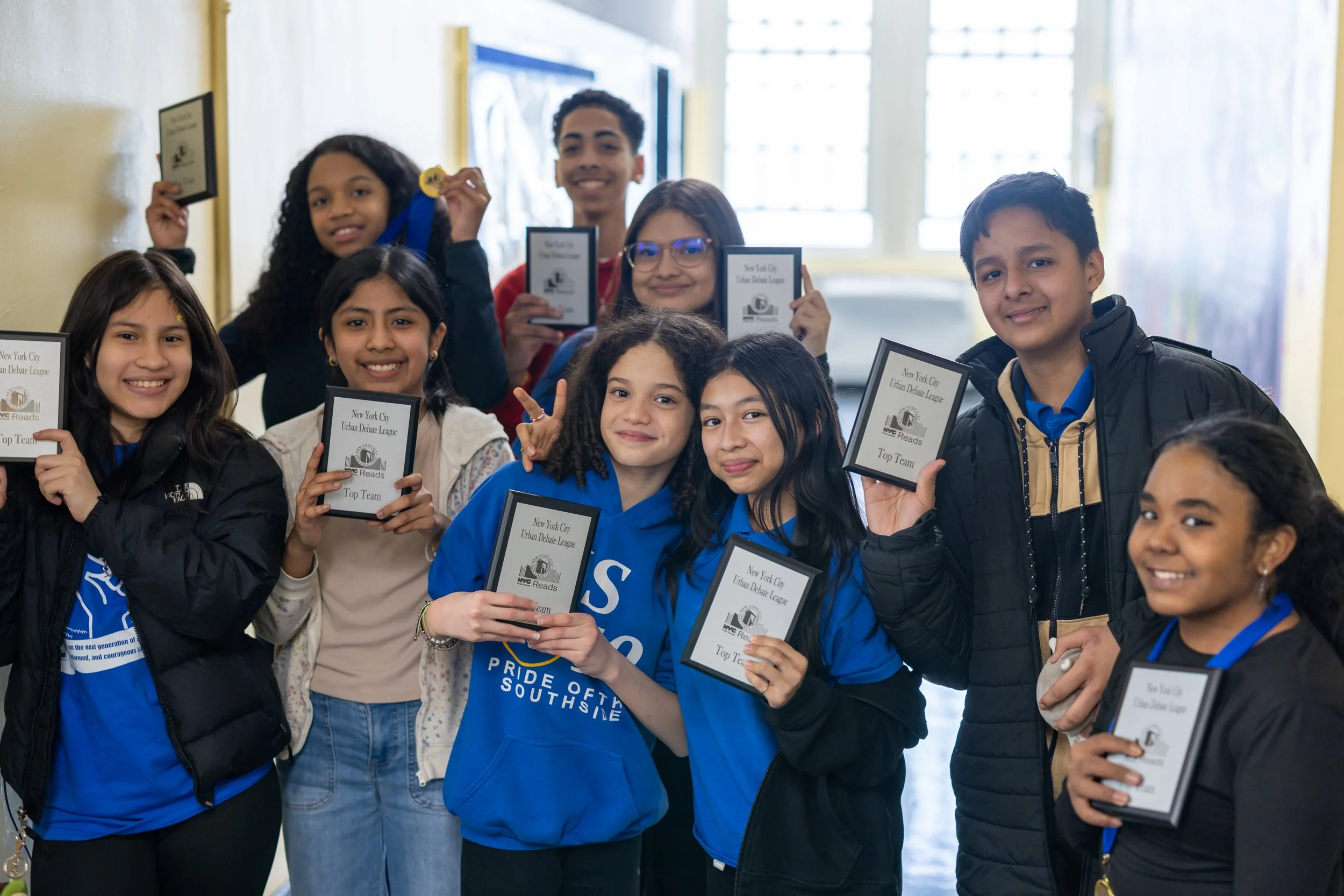 Group of diverse children holding awards and medals, celebrating a successful event in a school classroom.