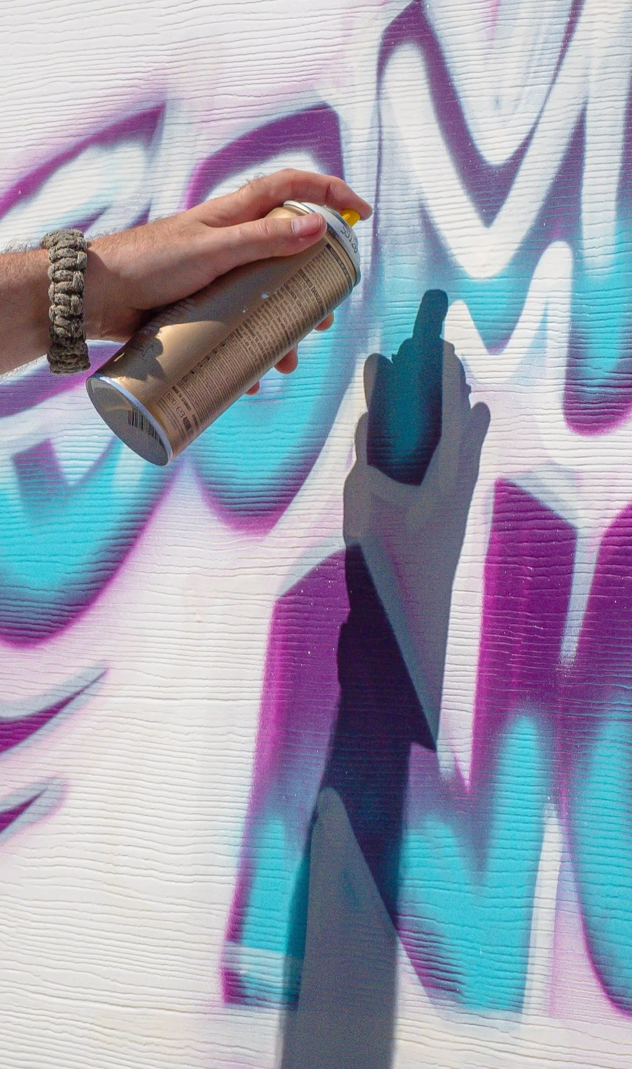 Person spraying graffiti onto a textured wall, creating a large colorful abstract design with purple, blue, and pink hues.