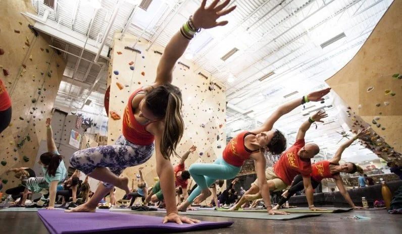 People practicing yoga on mats in an indoor climbing gym.