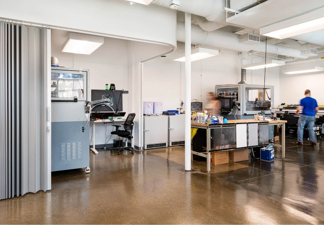 Laboratory workspace with scientific equipment, workbenches, and two people working.