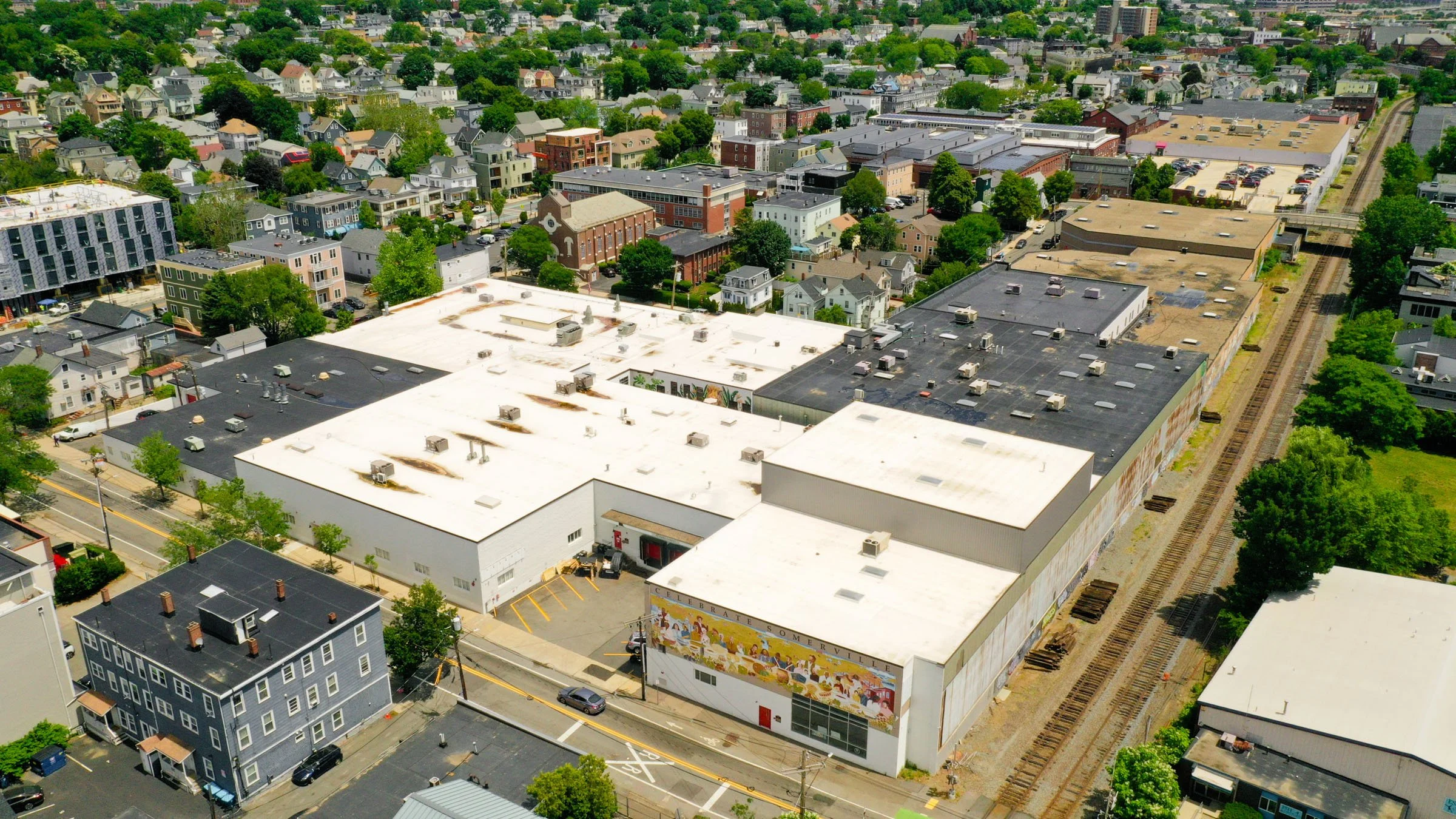 Aerial view of a city neighborhood with houses, commercial buildings, and a train track running along the right side.