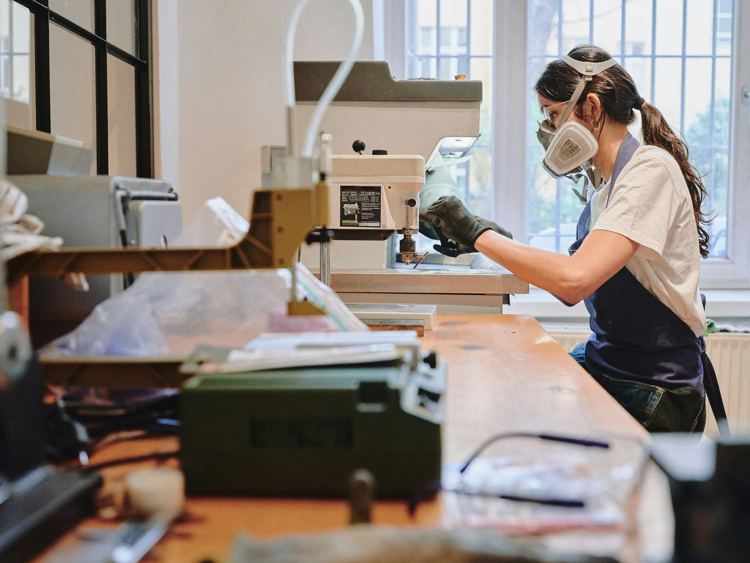 A woman wearing safety glasses, a mask, and gloves working in a laboratory with scientific equipment.
