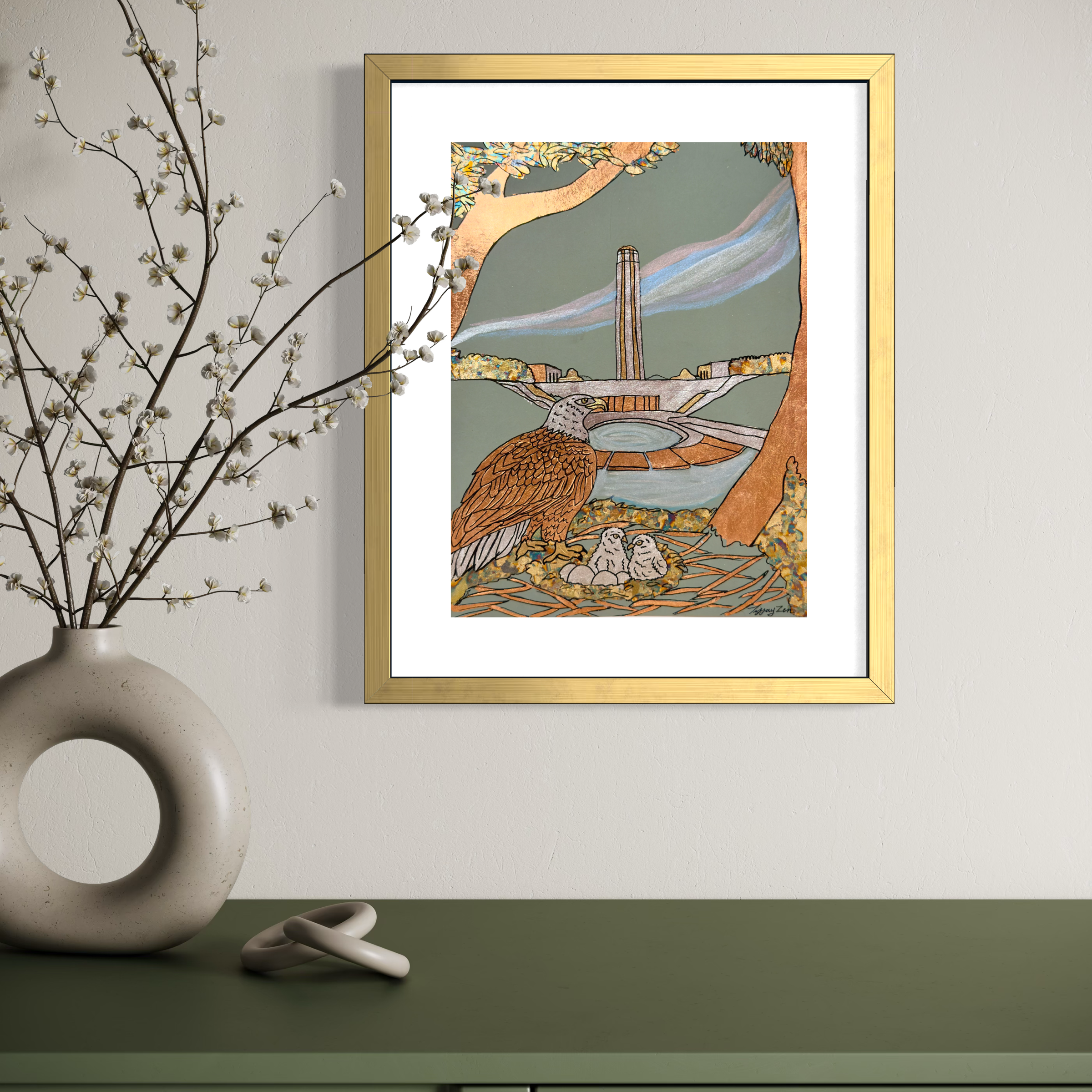 Colorful framed artwork depicting a bird, two small chicks, a circular water feature, tall building, and natural landscape with a tree, hanging on a beige wall, with a white vase with blooming branches and a ceramic ring on green tabletop.