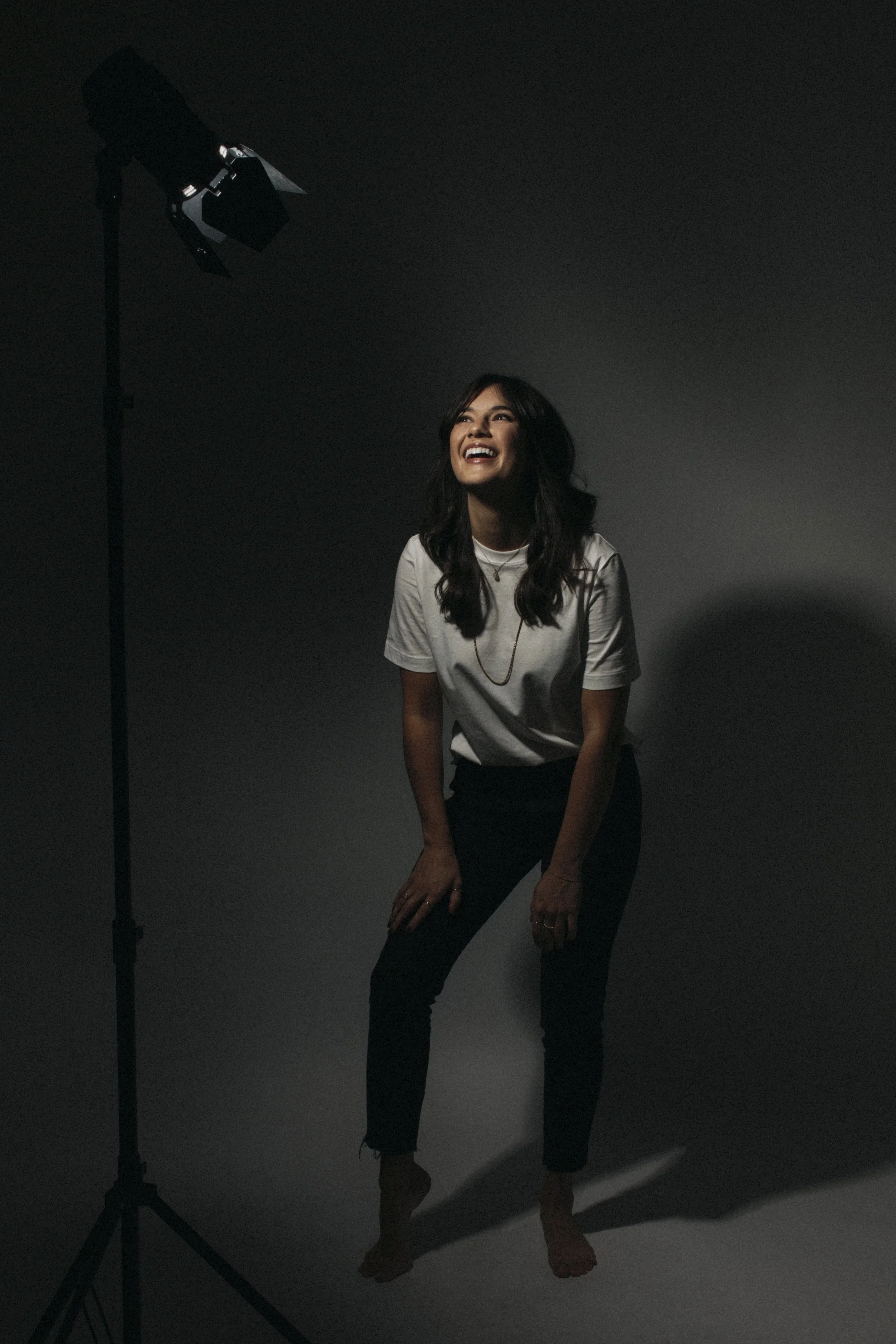 A woman smiling and laughing while posing for a photo in a studio with a single light.