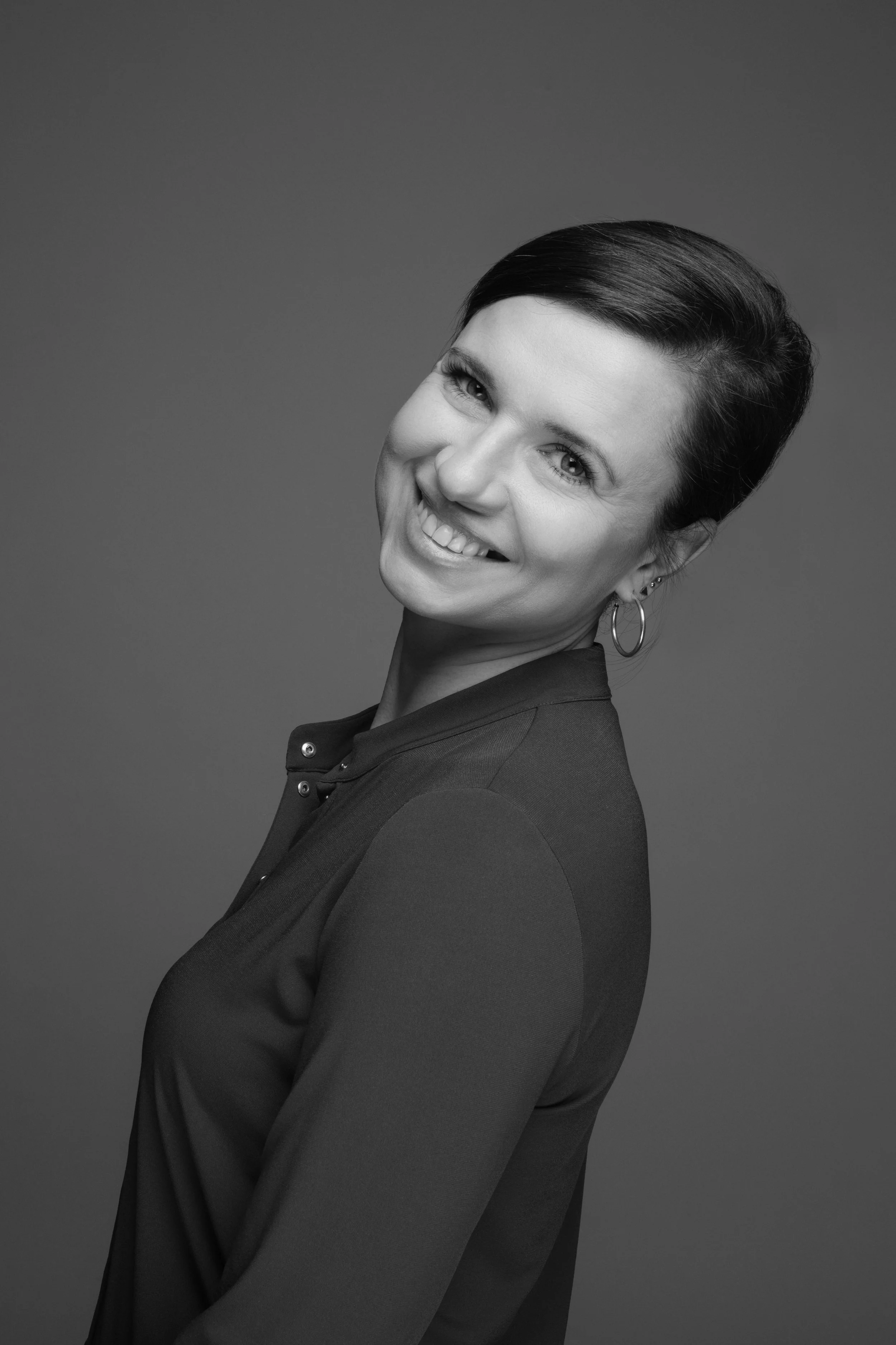 Black and white portrait of a smiling woman with short dark hair, wearing hoop earrings and a dark top against a plain background.