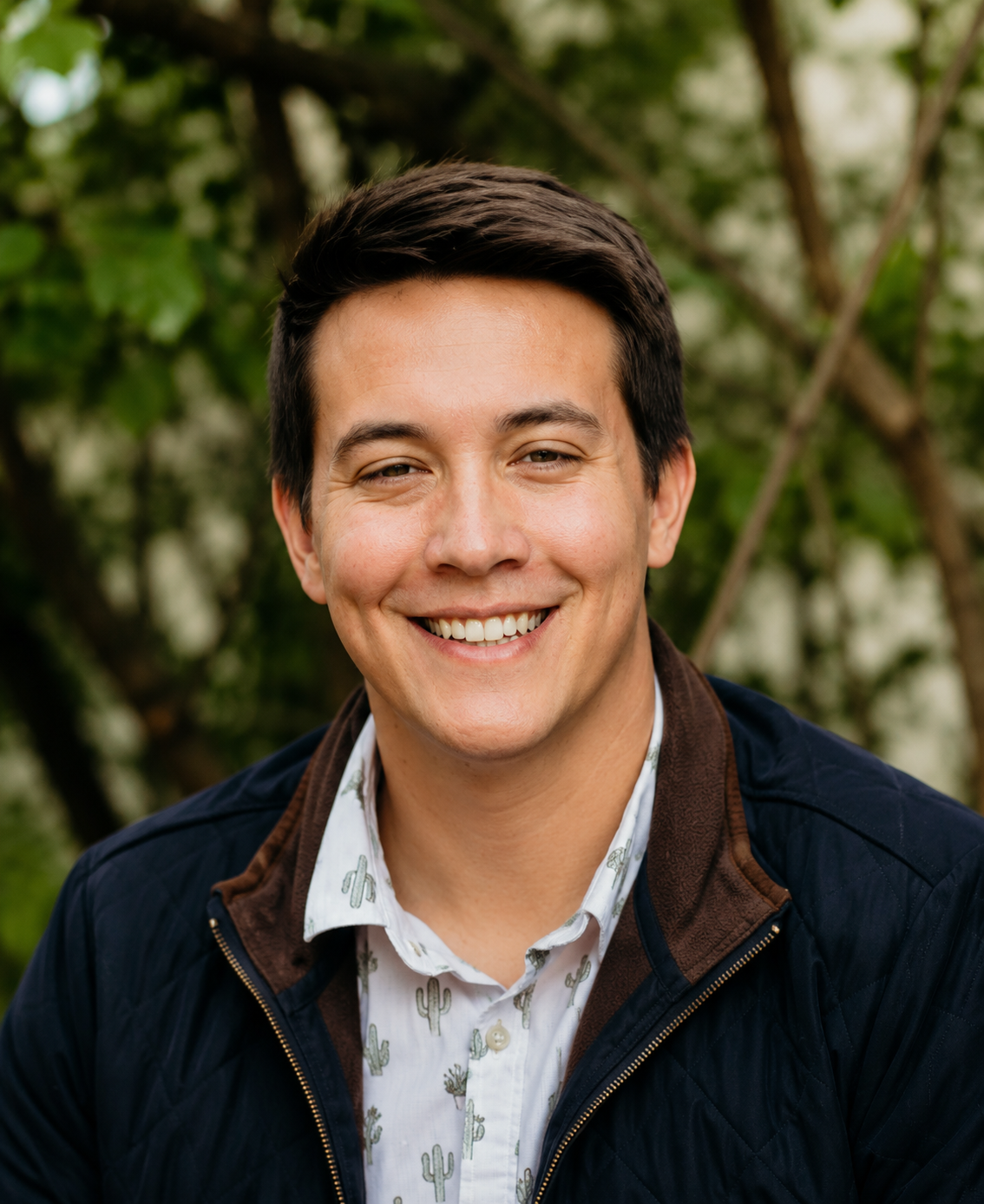 Young man smiling outdoors with green foliage background