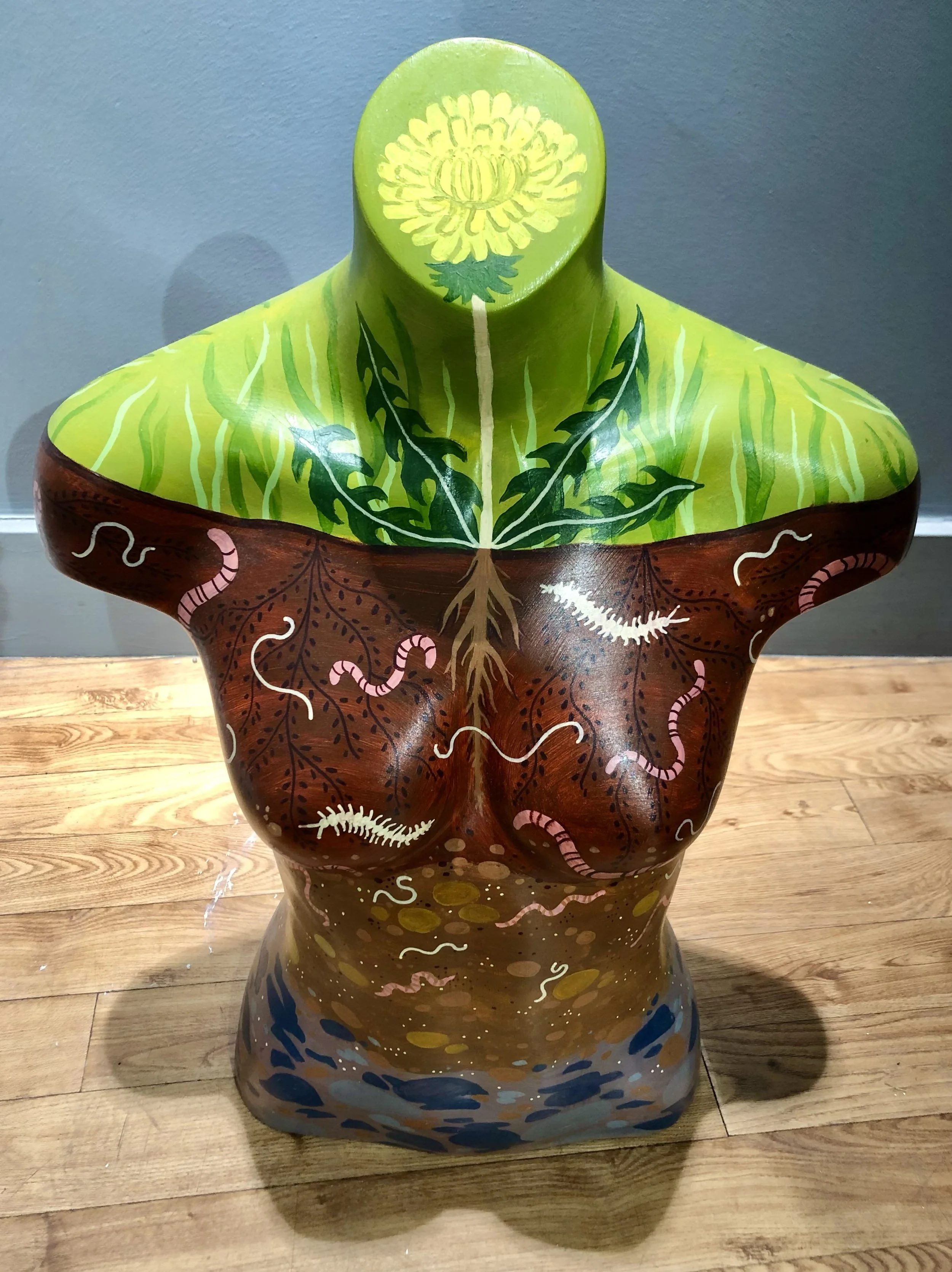 A female mannequin torso painted with a dandelion in place of the head and soil below. Worms and centipedes wriggle between the roots and rocks. The artwork is by Hayley Wells and was part of the Chelmsford Art Trail 2022.