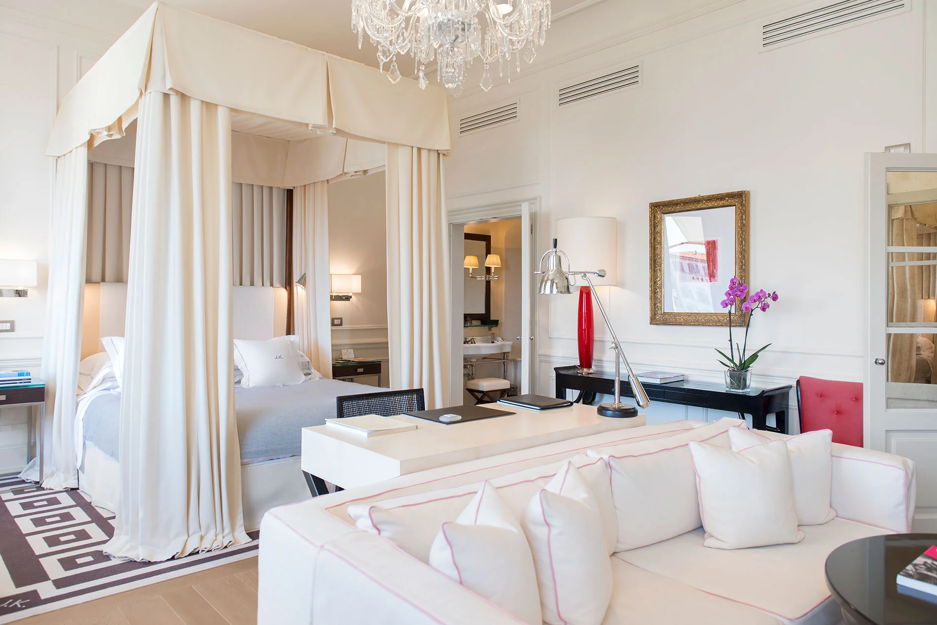 Luxury hotel room with four-poster bed, sitting area, and elegant decor.