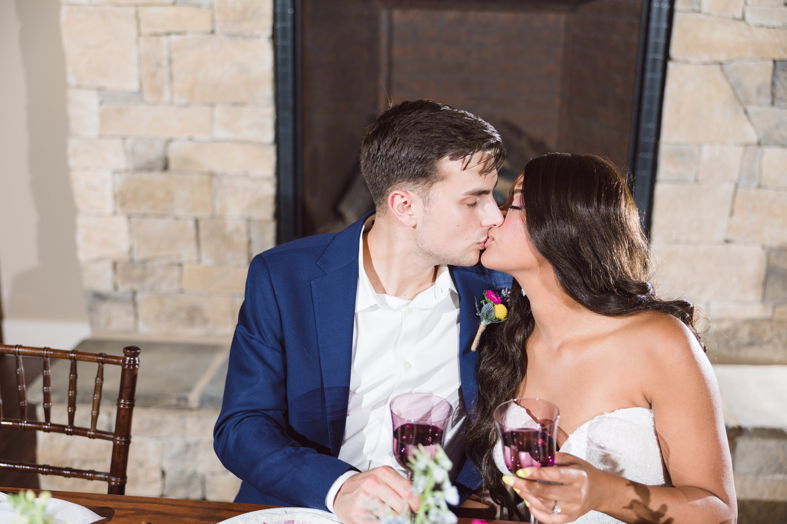 couple kissing at The English Barn wedding venue while holding wine goblets
