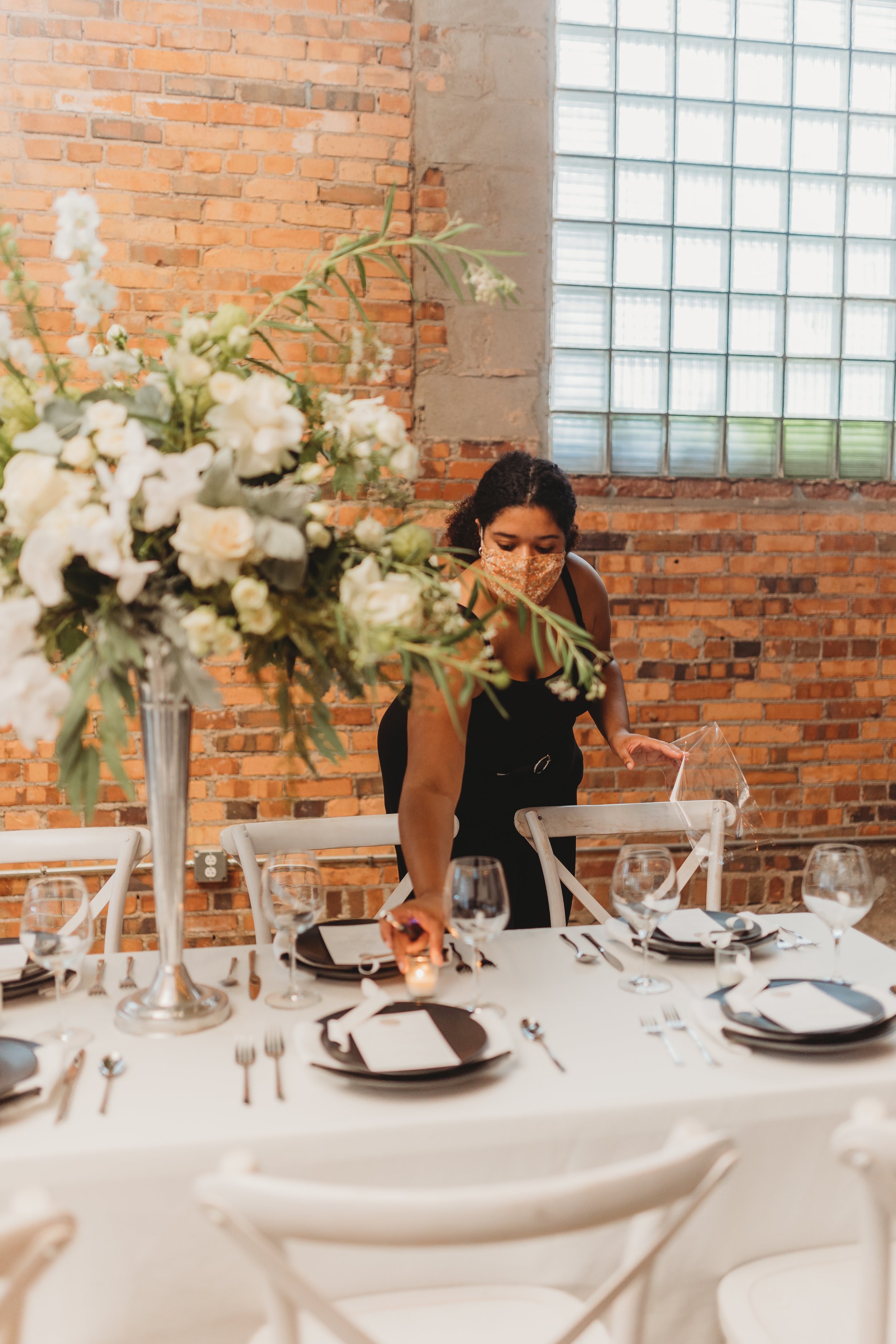 Sofi Melvin, Kansas City wedding planner, placing a lit tealight candle on a table with black and white decor and a large floral arrangement
