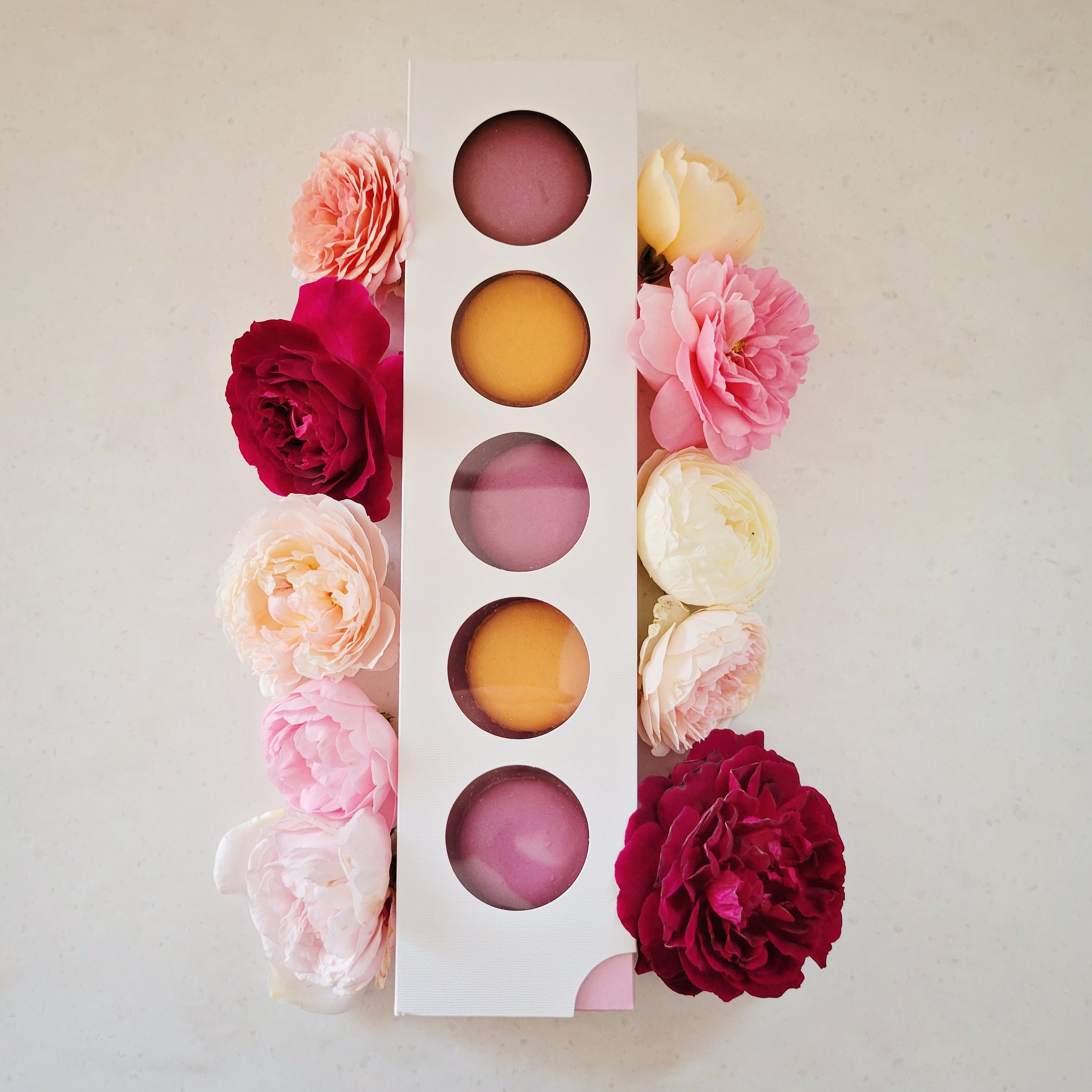 Pink and orange macarons in a decorative box surrounded by flowers