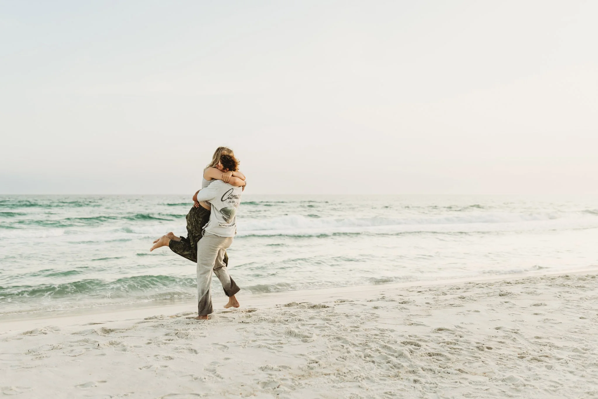 A woman jumping into the arms of a man on the beach at sunset