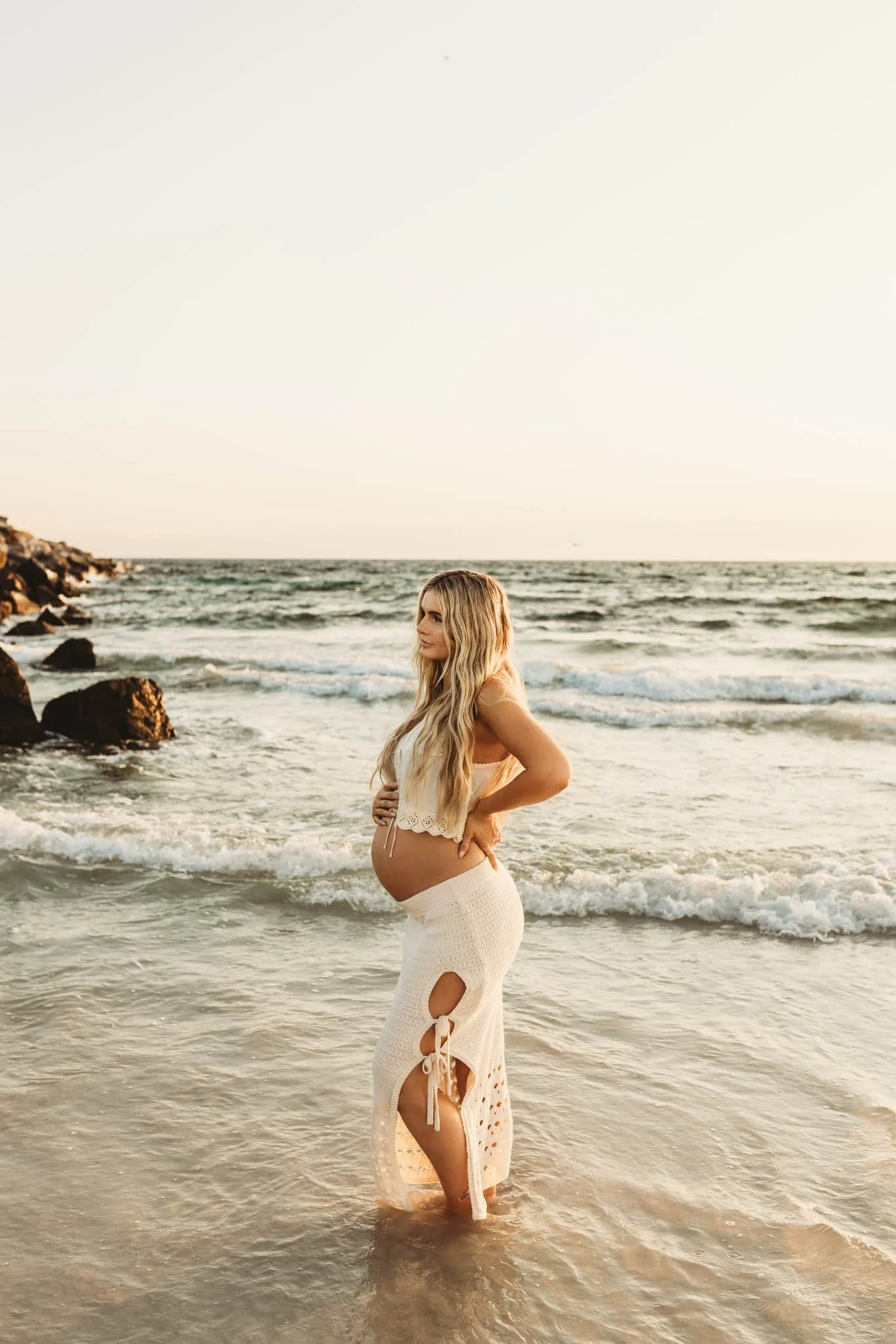 Pregnant woman with her hand on her belly while standing in the waves at the beach