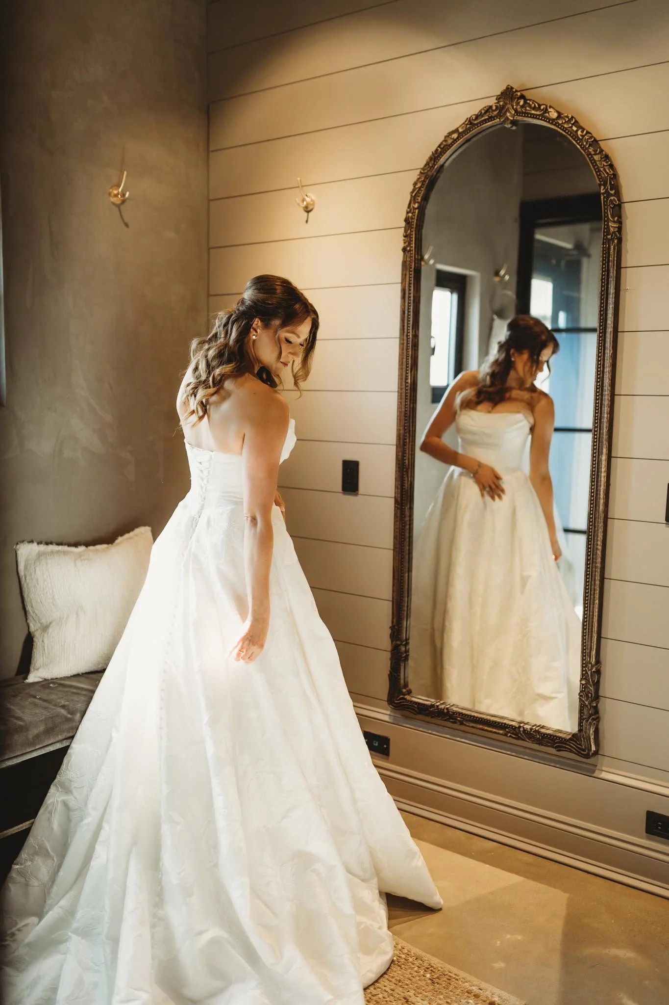 Bride getting ready in a bridal suite at The Heritage House. A large golden mirror shows her reflection on a shiplap wall.