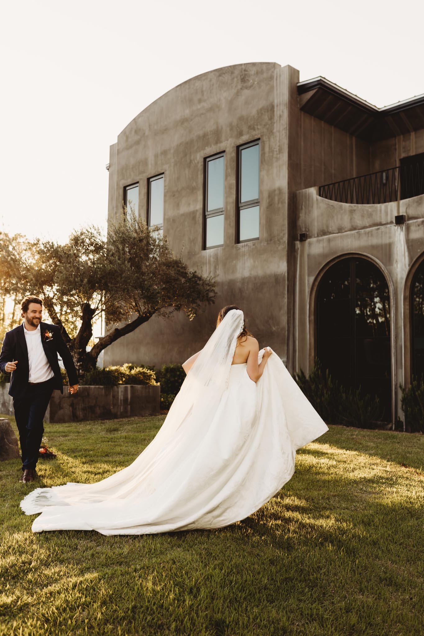 Bride and Groom being playful for portraits outside in front of a modern concrete European inspired wedding venue.