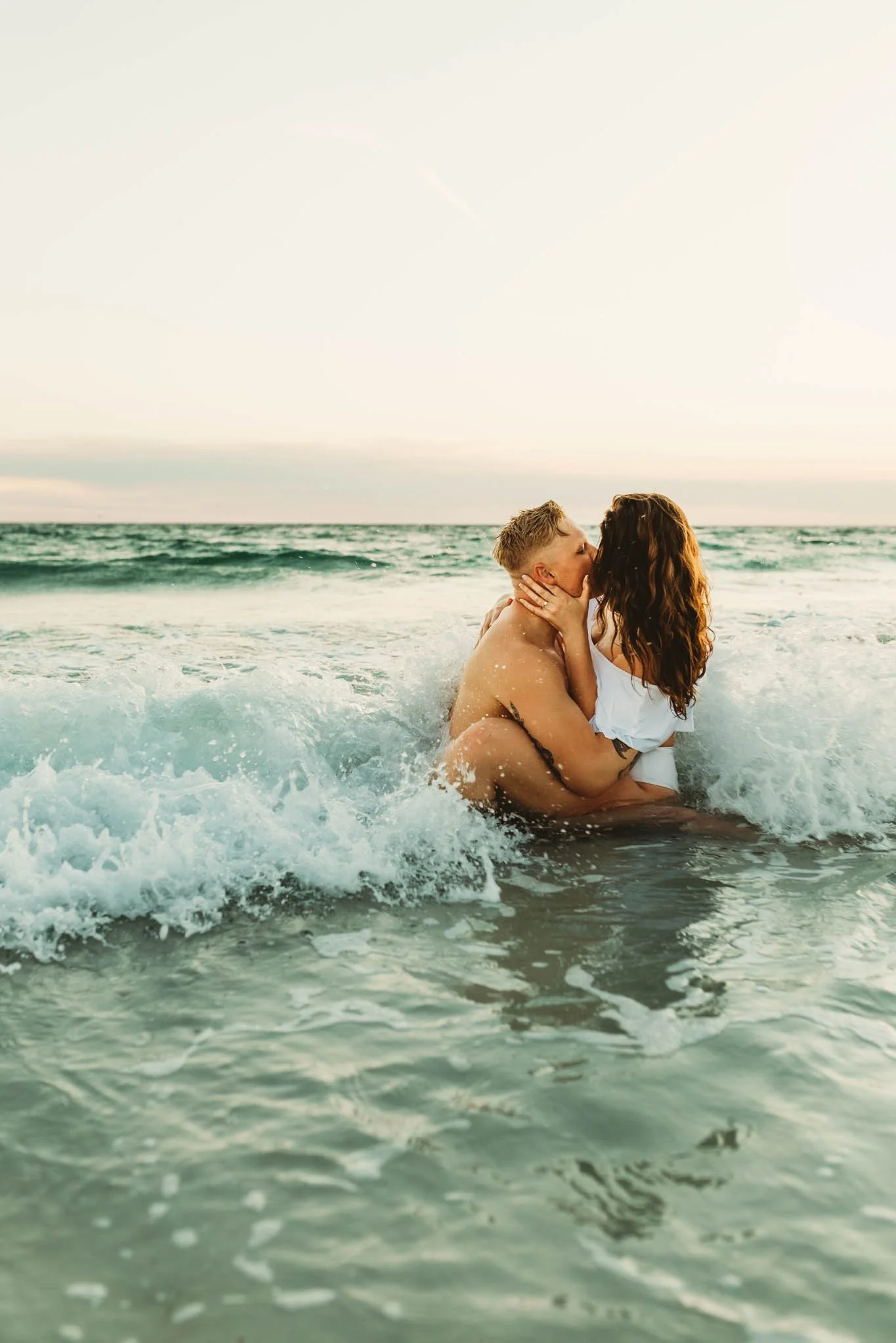 Couple sitting in the waves of the beach kissing at sunset