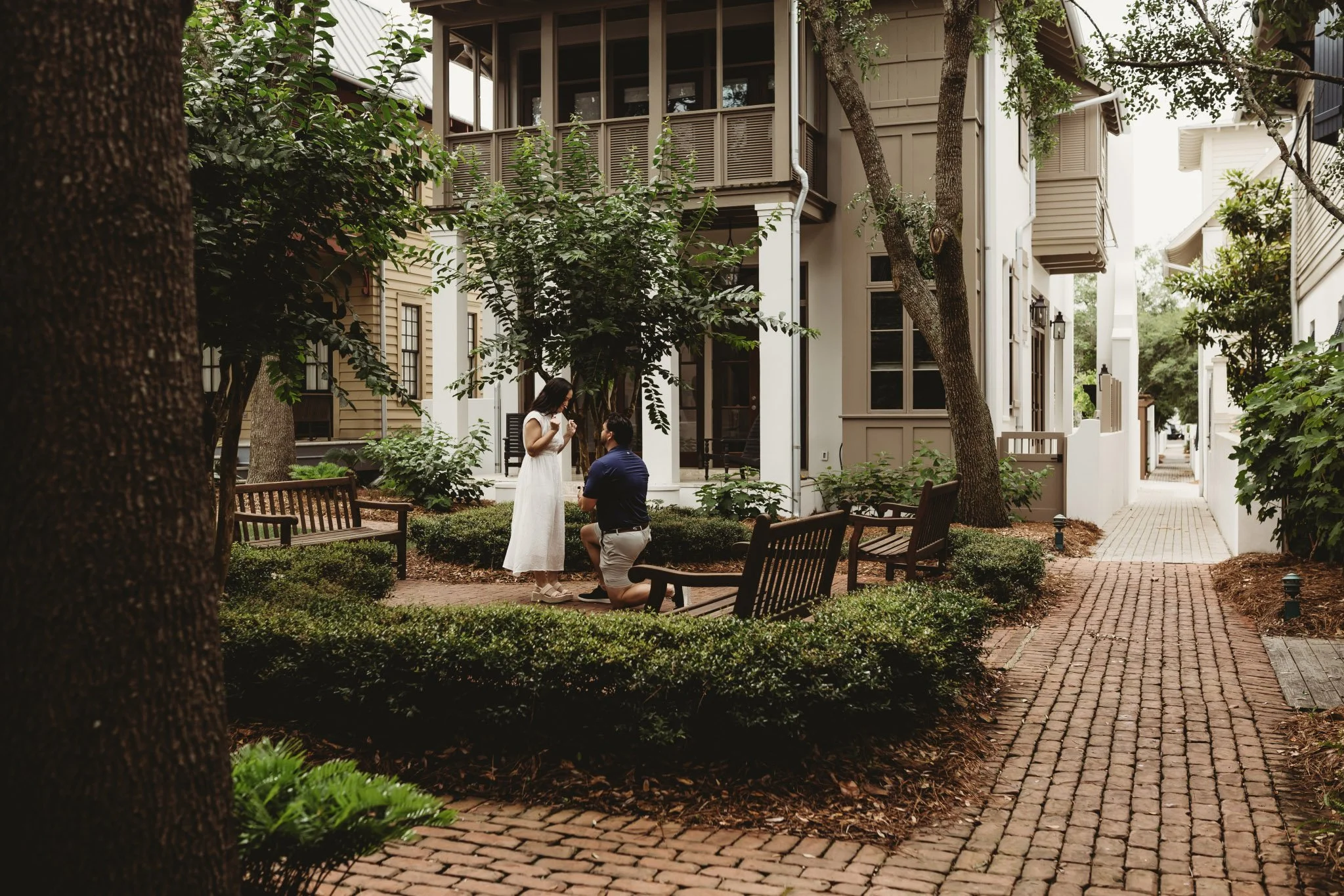 A man on one knee proposing to a woman in a lush green courtyard along 30A