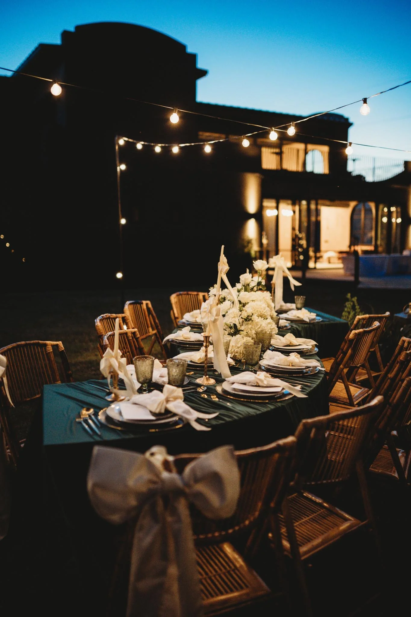 A dark green tablescape set up under twinkling cafe lights. The silhouette of The Heritage House is in the background.