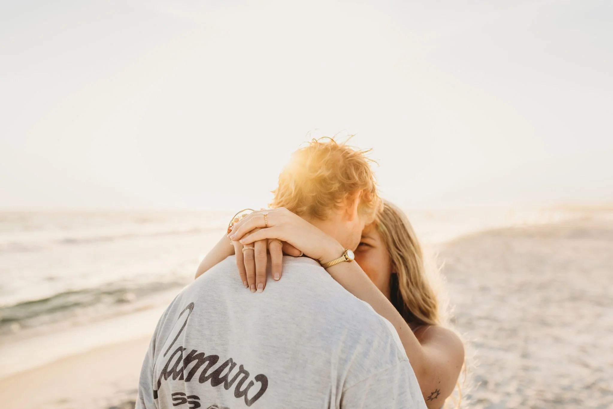 Golden hour sunset photo of a newly engaged couple on the beach holding each other