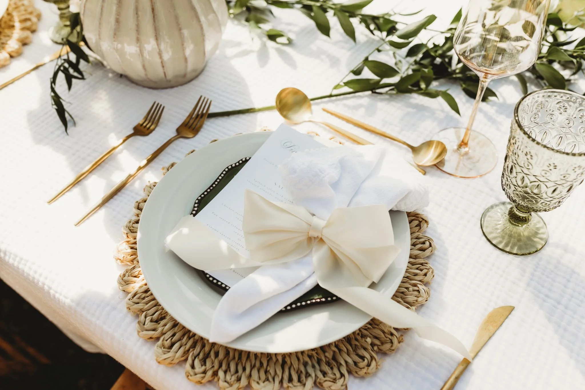 Luxury tablescape with cream colored linens, gold utensils and green touches