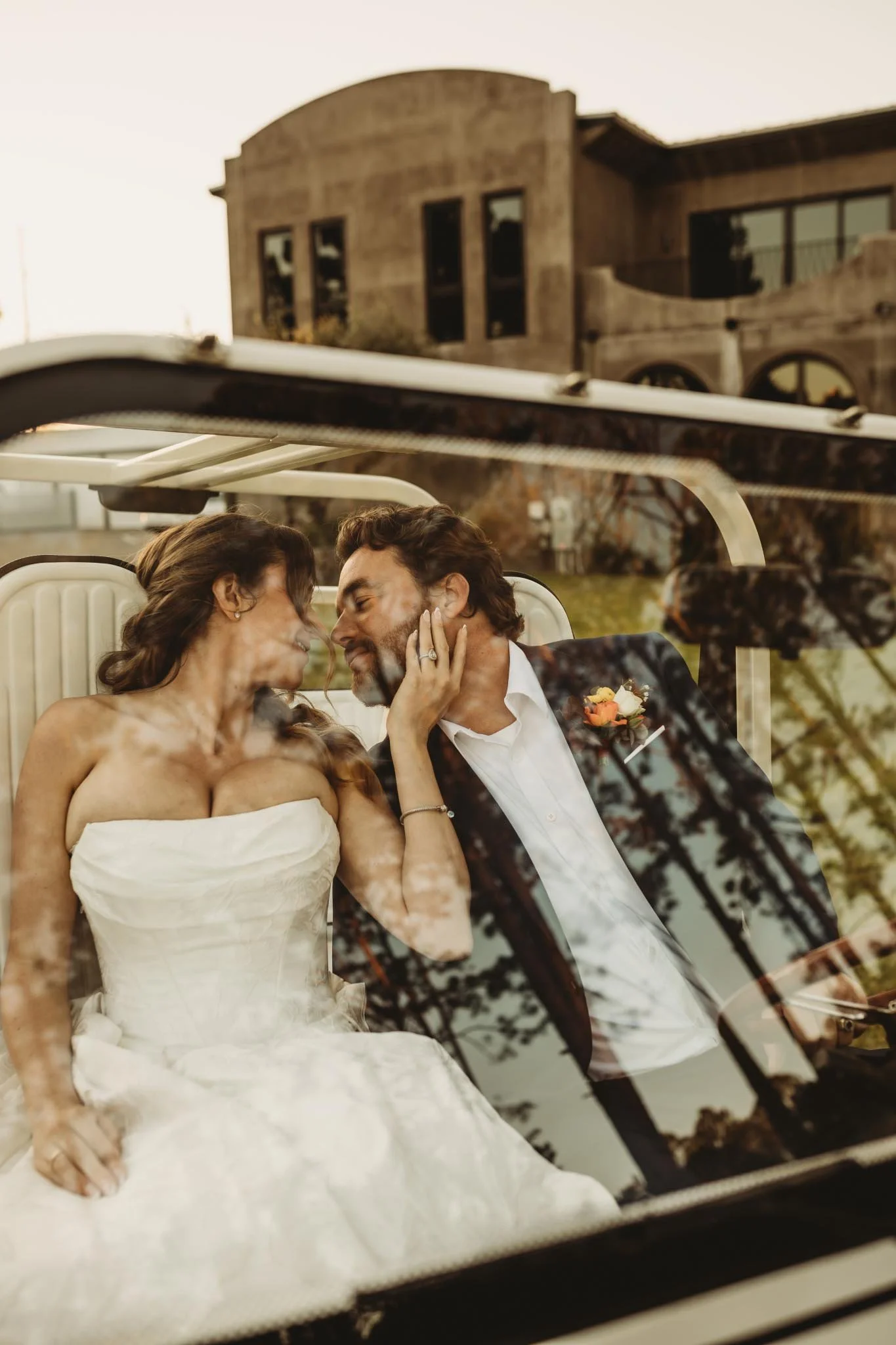 Photo through the windshield of a bride and Groom about to kiss inside of a getaway car