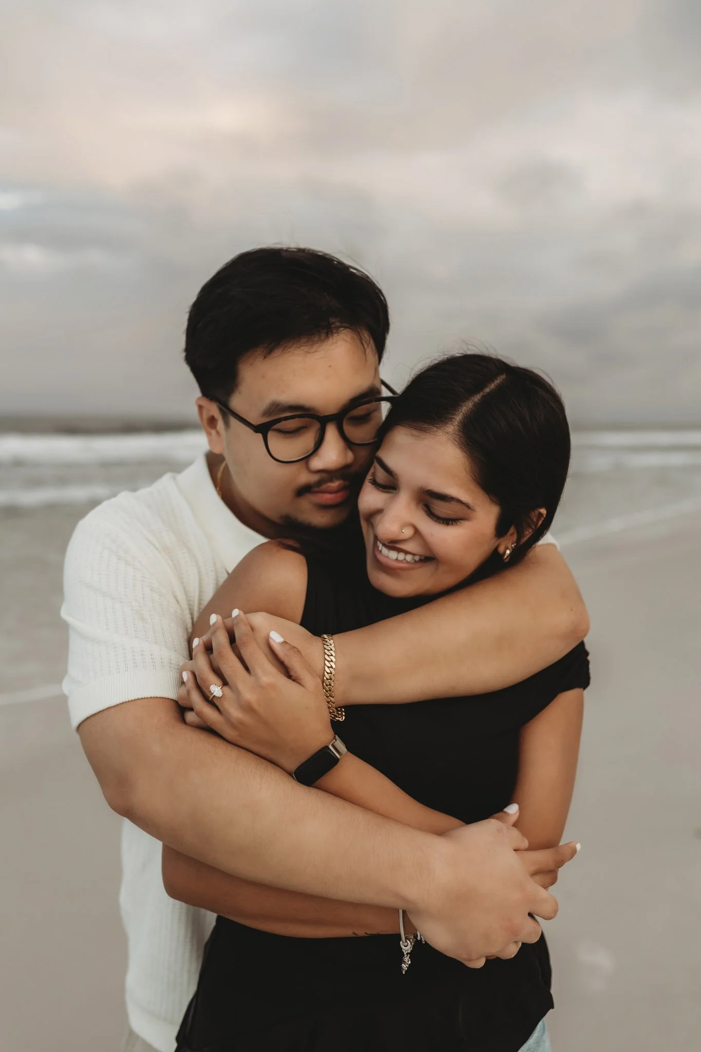 Man and woman embracing on the beach, smiling and showing a diamond ring