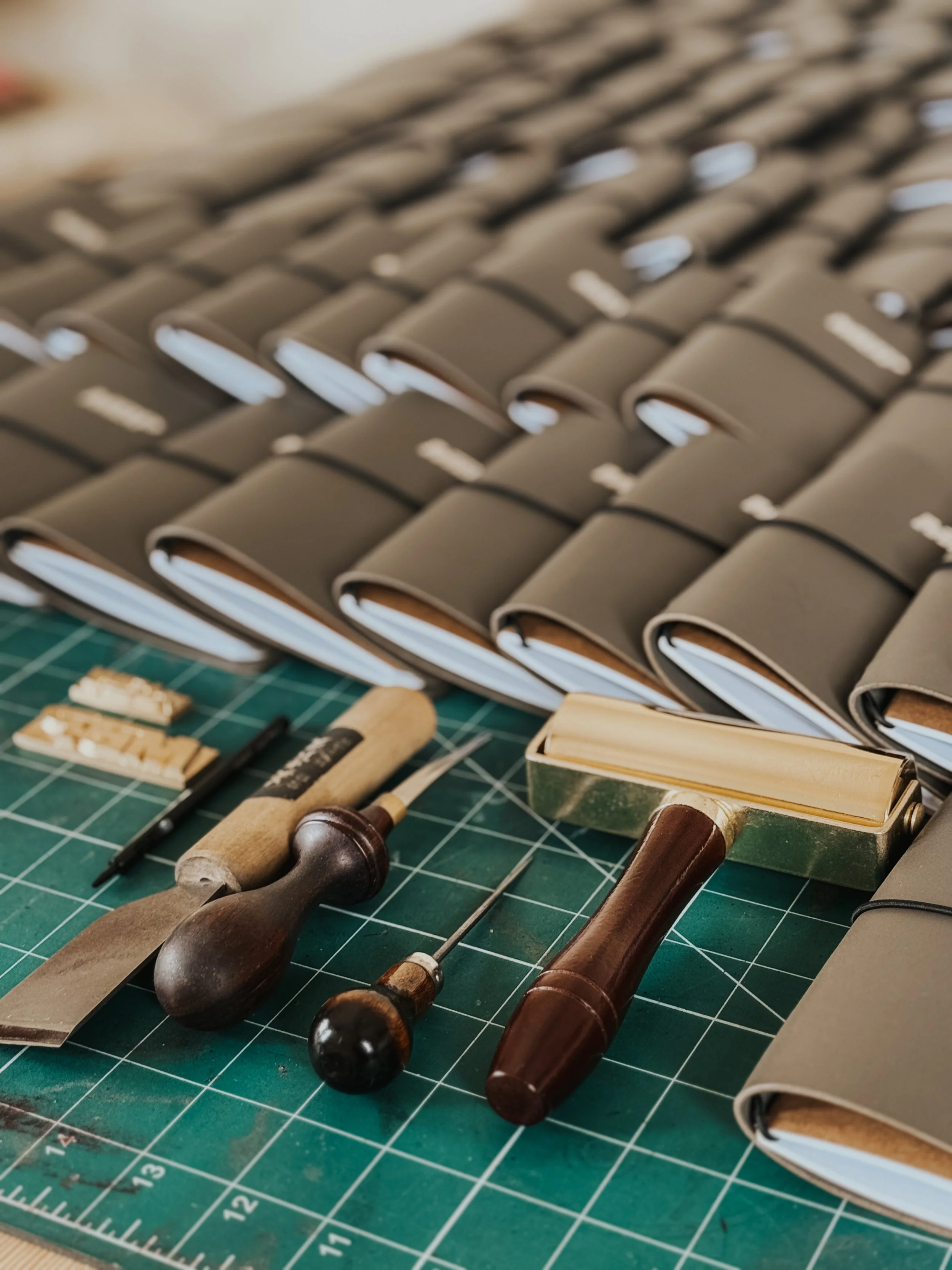 A close-up photo of woodworking tools including chisels and hammers on a green cutting mat, with books stacked in the background.
