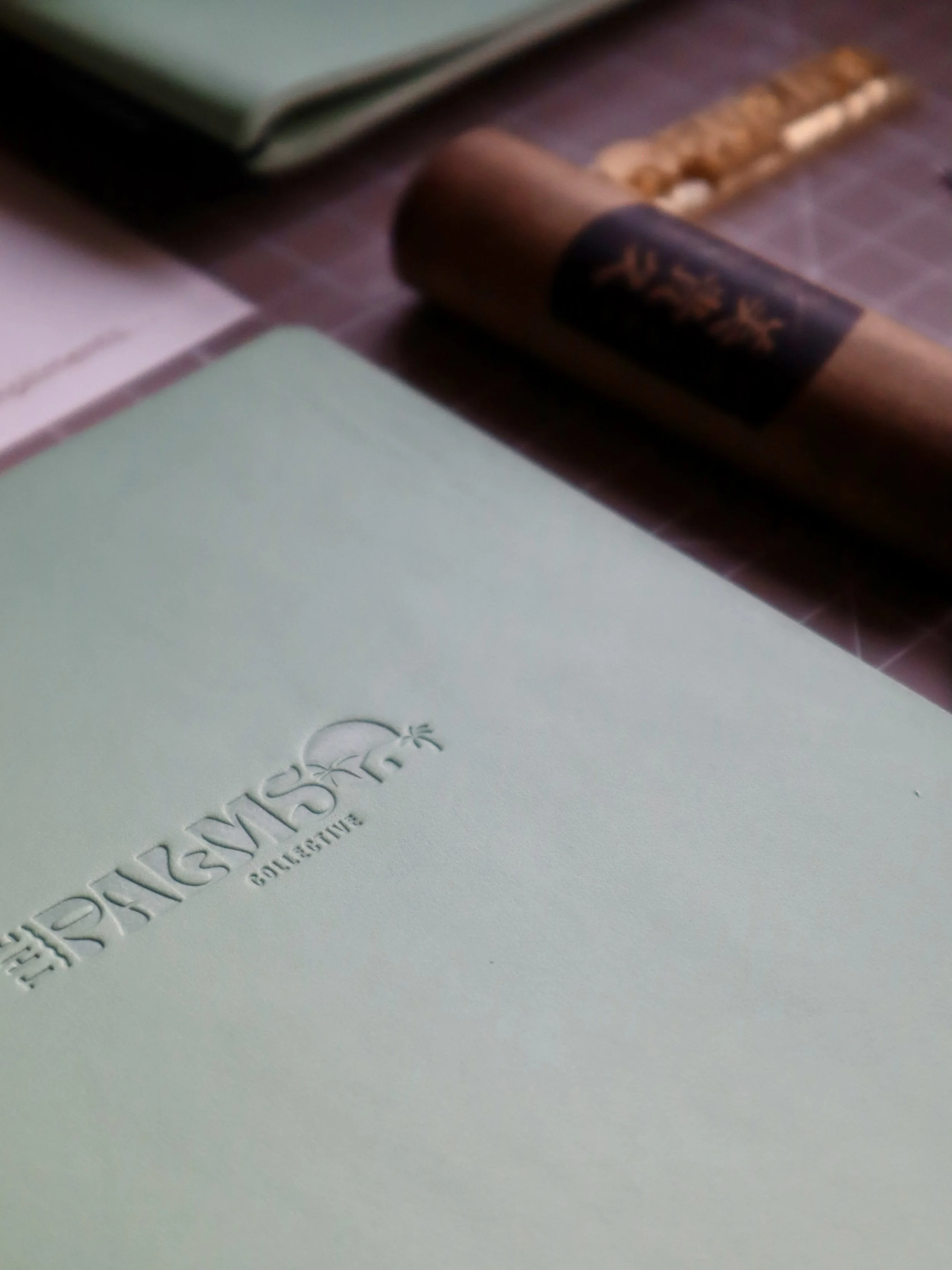 Close-up of a light green notebook with embossed text, alongside a brown cigar and another book in the background.