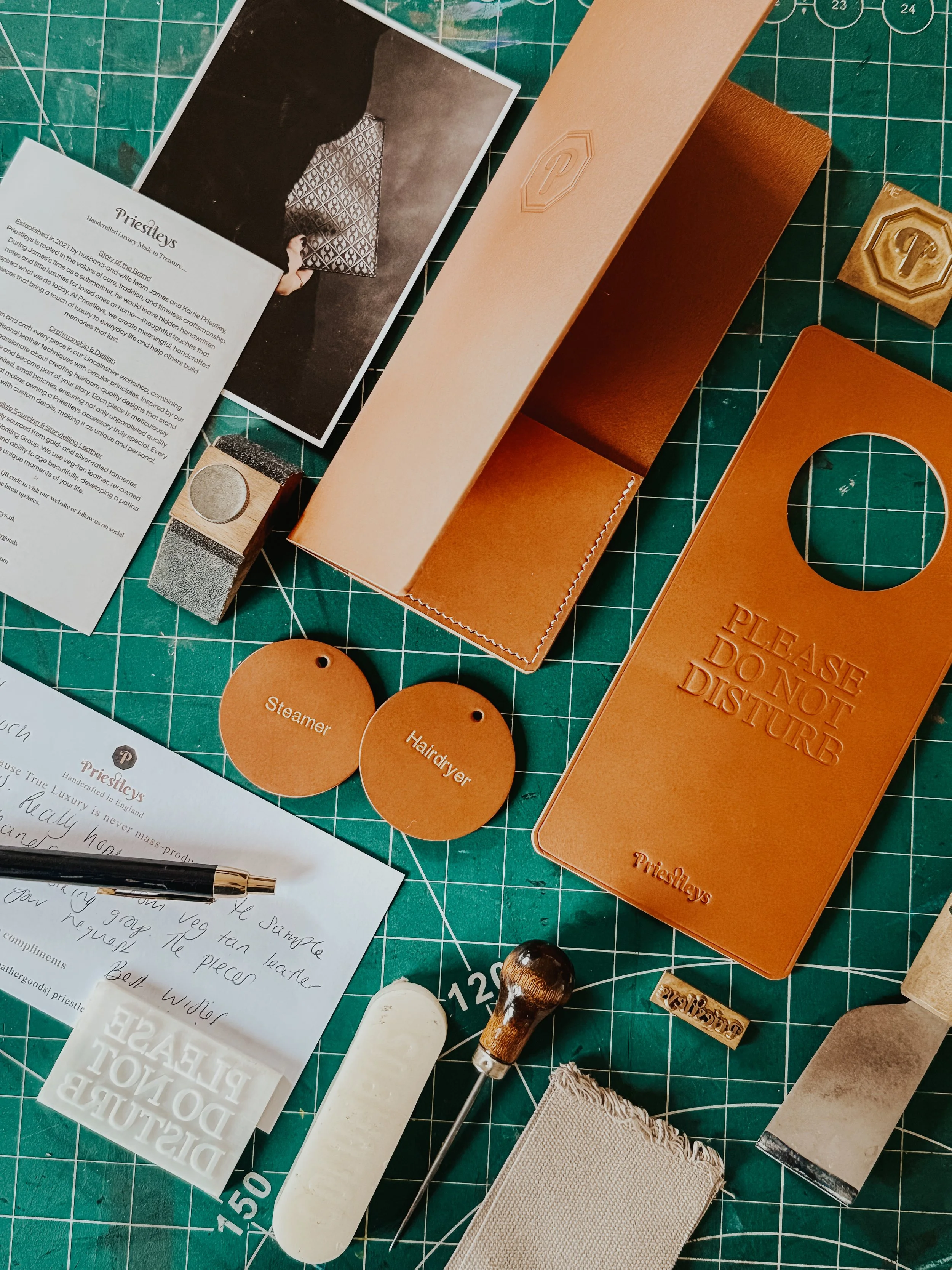Various leather crafting tools and materials on a green cutting mat, including leather pieces, a stamping tool, labels, and instructions for leather projects.