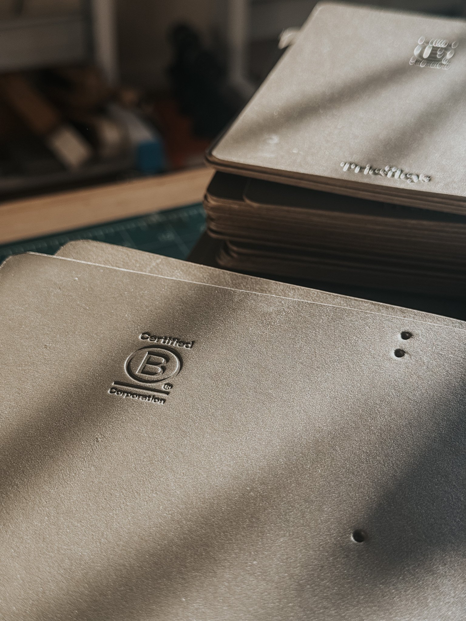 Close-up of a stack of business cards with a beige textured surface, featuring a logo with an oval shape and letter 'B' in the center, along with some small black dots.