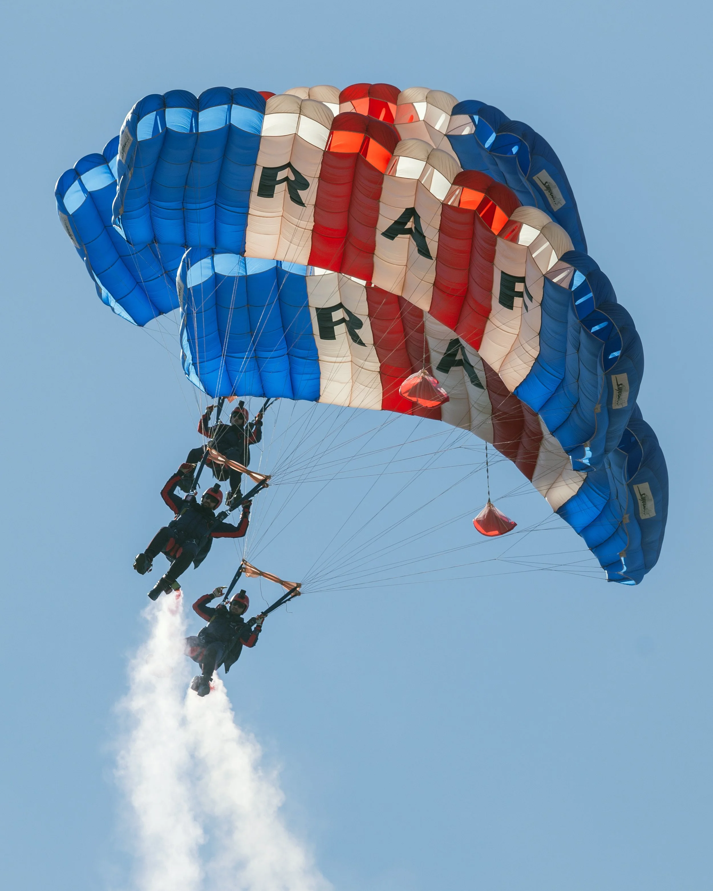 Three skydivers descending with a parachute featuring red, white, and blue colors and the word 'USA'.