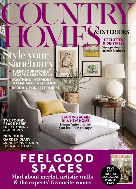 Cover of a magazine titled 'Country Homes & Interiors' featuring a cozy living room with a gray armchair, a yellow pillow, a wooden side table with a large white lamp, and framed artwork on the wall.