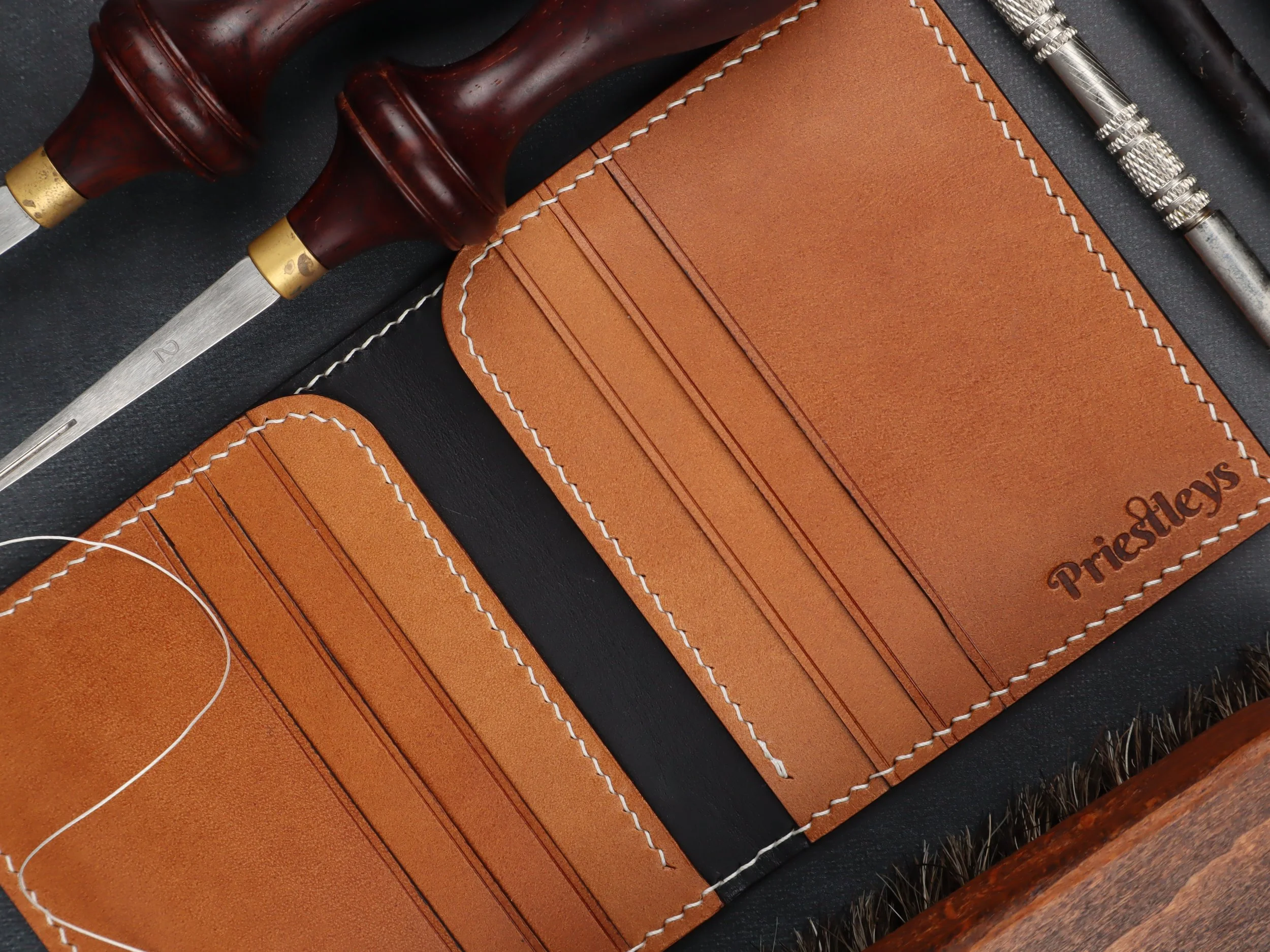 A leather wallet with card slots and the brand name Pastor's engraved, surrounded by woodworking and leatherworking tools.