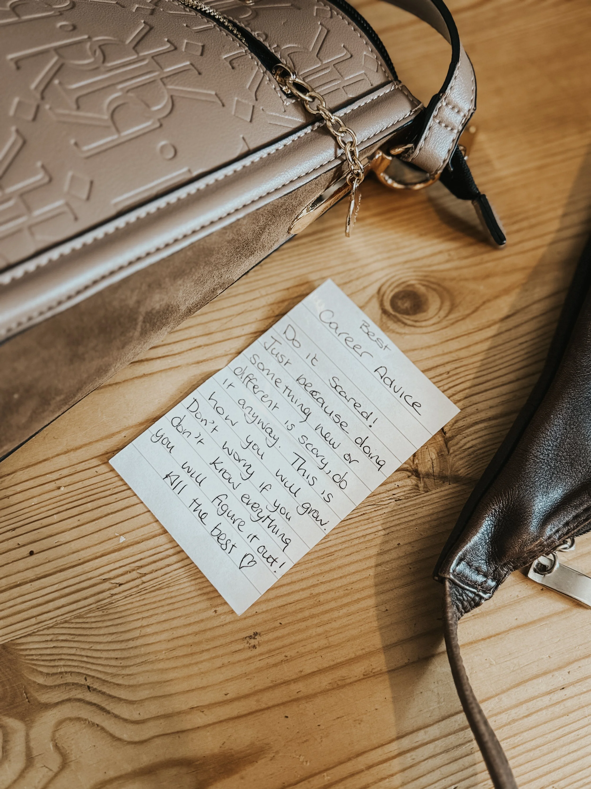 A handwritten note titled "Best Caree Advice" on a wooden surface, with a beige handbag with embossed design and a chain strap positioned above the note, and part of a brown bag visible on the right.
