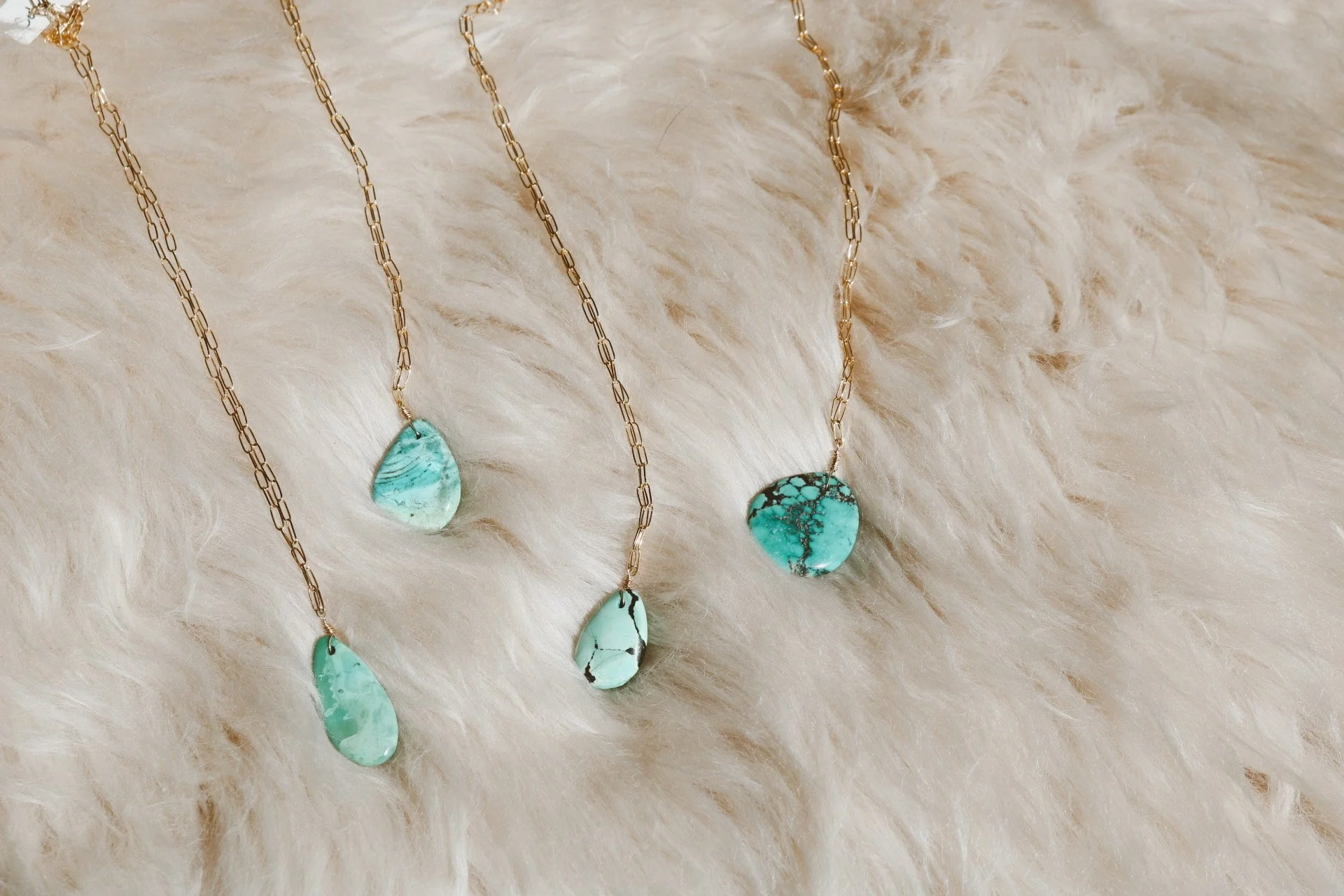 Three necklaces with turquoise gemstone pendants on a plush, cream-colored, furry surface.