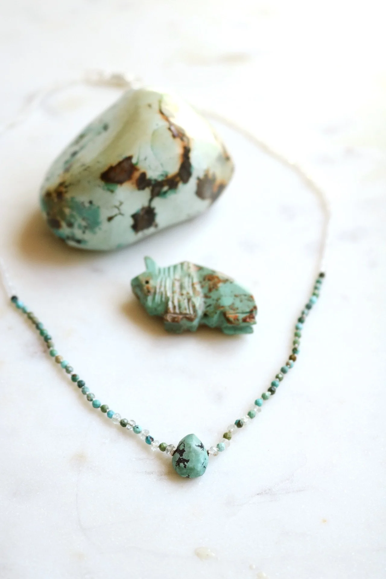 Turquoise jewelry set including a necklace with a turquoise stone pendant, a large turquoise stone with brown and black veining, a small turquoise animal figurine, and a small turquoise and brown beaded item.