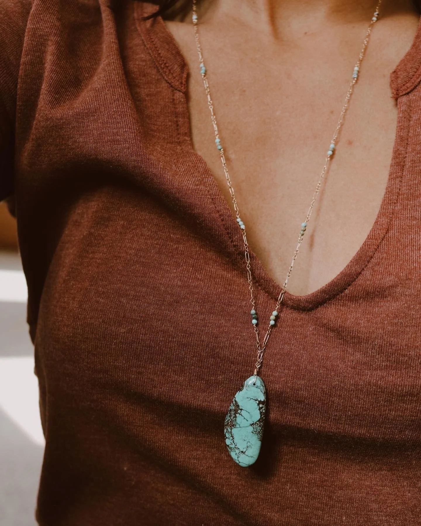 A woman wearing a rust-colored top and a long turquoise stone pendant necklace