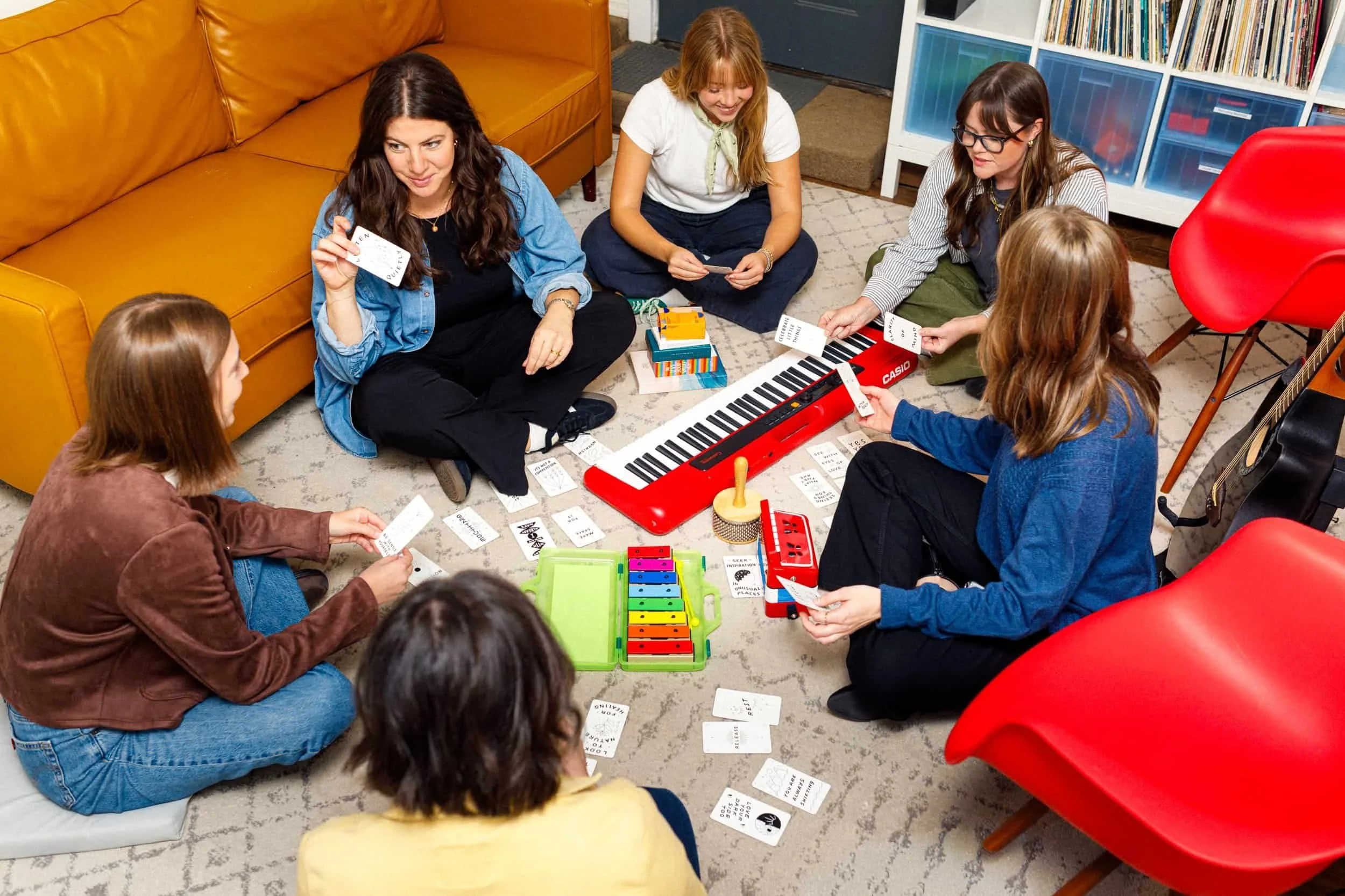 Six women sit in a circle on a carpet, playing a music-themed card game—staff wellness Nashville in full swing.