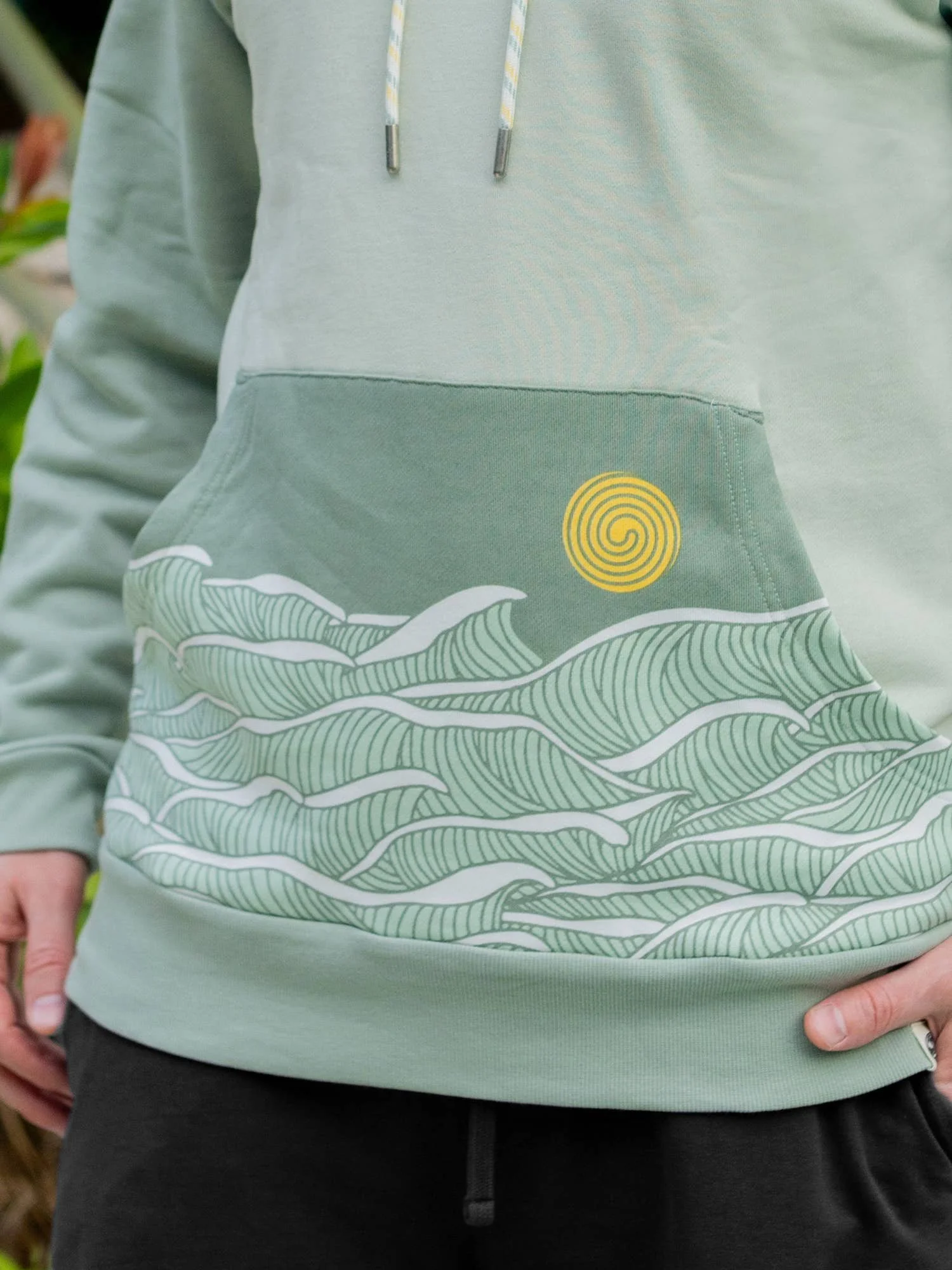 Happy Earth Beach Break Hoodie is made from 100% GOTs cotton and has the graphic of waves and the sun on a sage green ground.