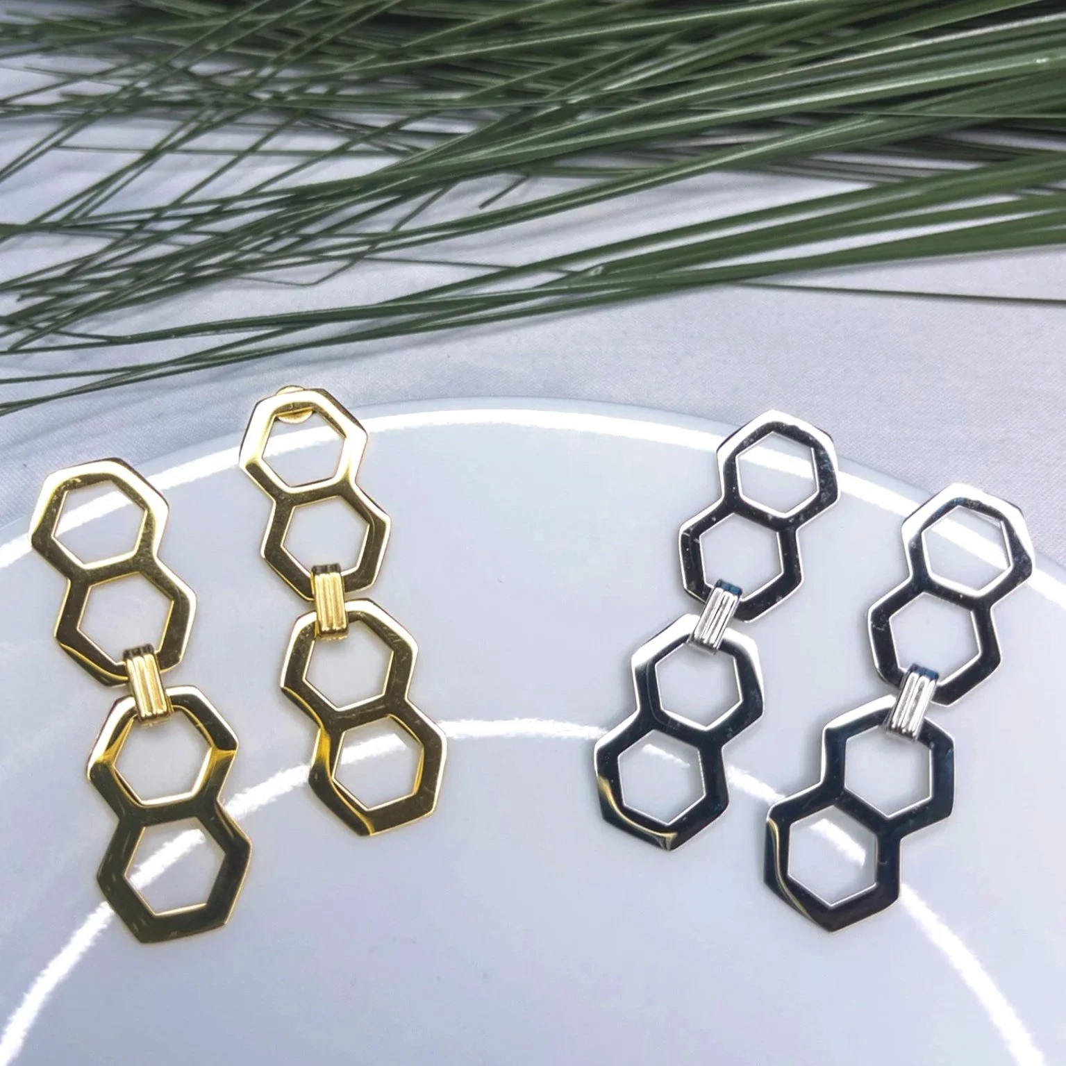 Two pairs of geometric hexagon-shaped earrings, one pair in gold and the other in silver.