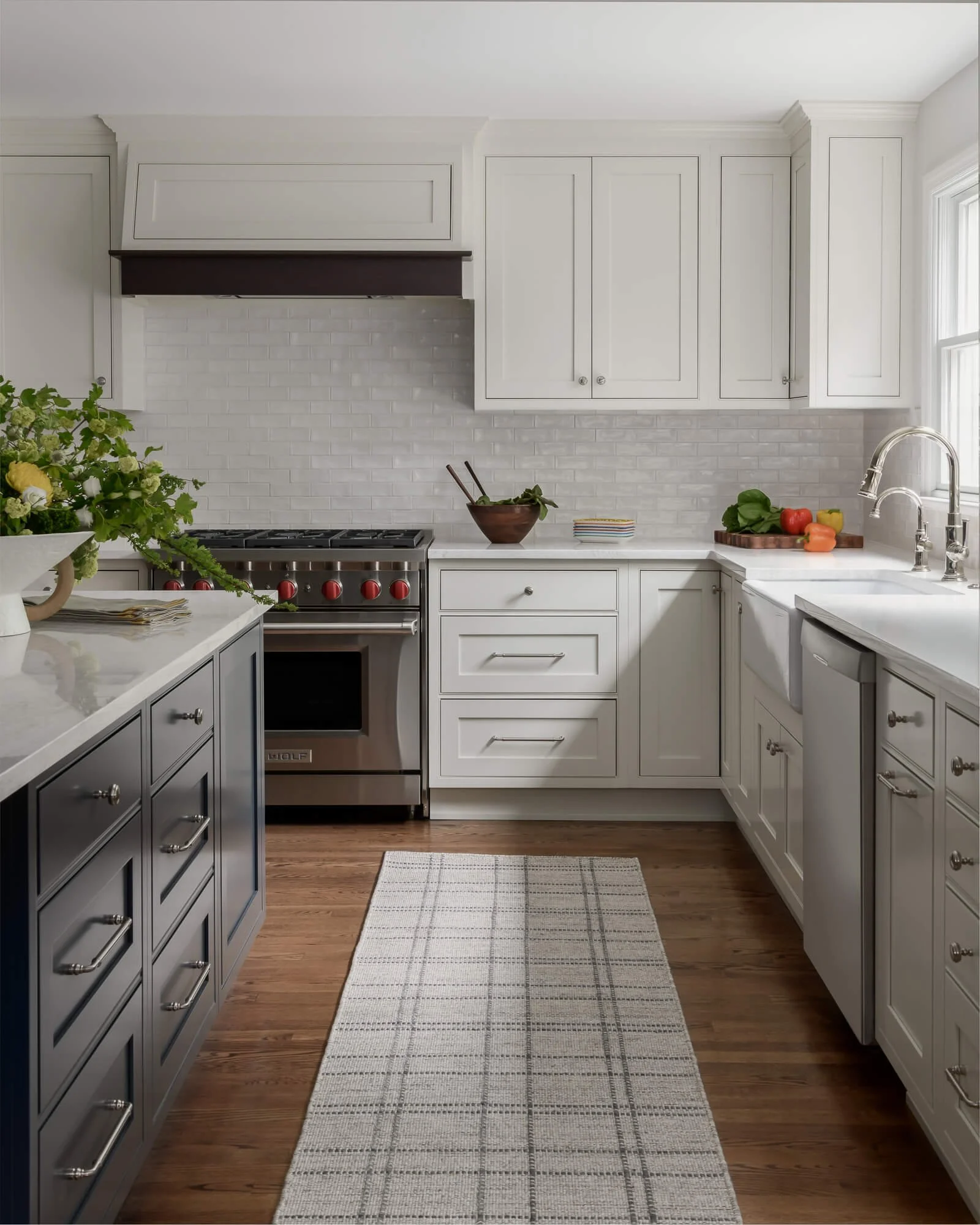Kitchen renovation by Elements Interior Design Studio in Westfield, NJ featuring white cabinets, backsplash and countertops. Theres a runner on the floor and a large gray island.