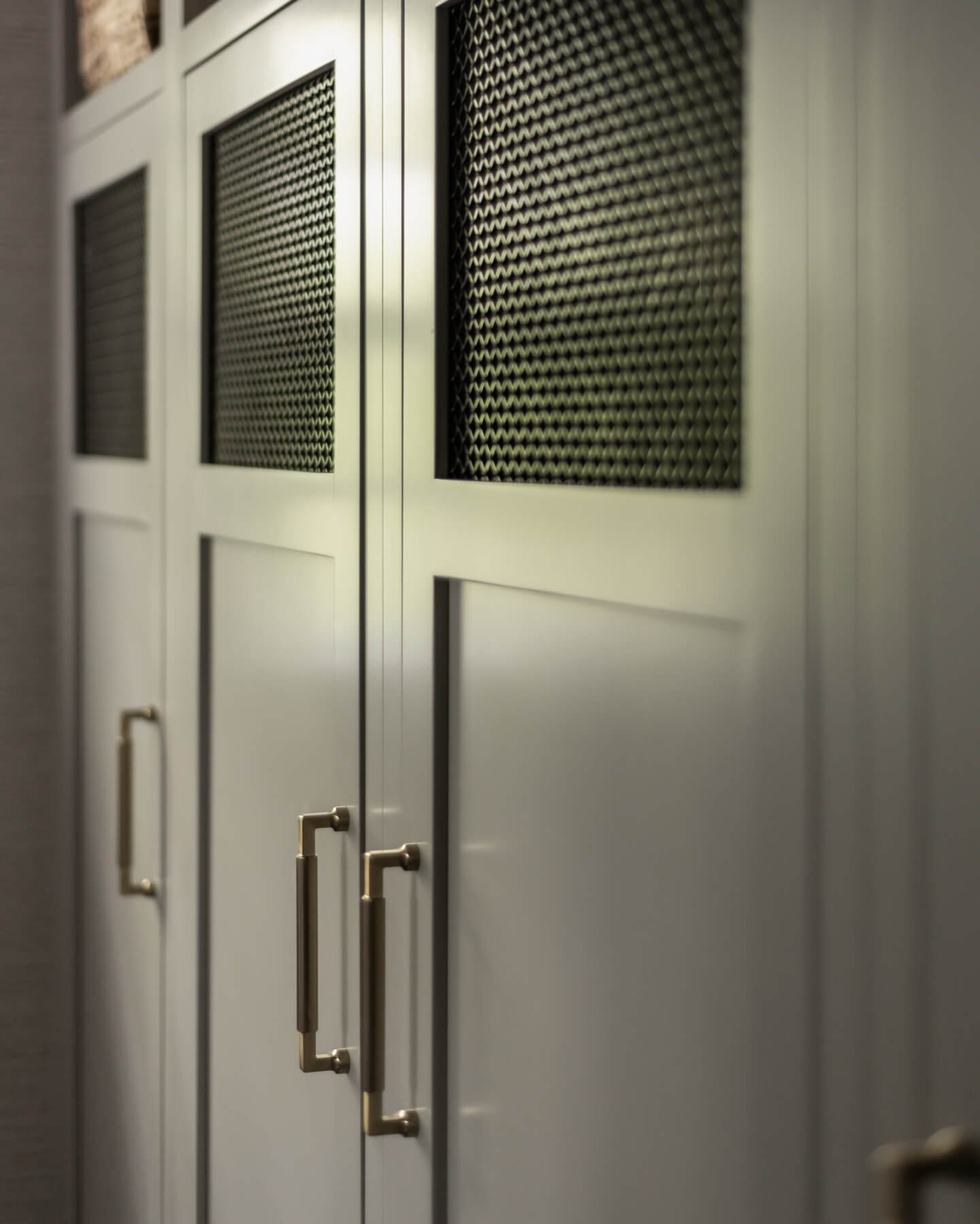 Close up of greige cubbies with mesh inserts and brass hardware in a mudroom renovation in Cranford, NJ by Elements Interior Design Studio.